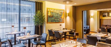 A restaurant with tables set for dining, a large window with curtains, a painting on the wall, and a potted plant.