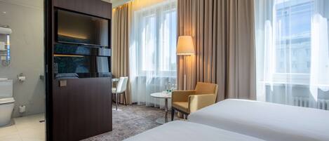 Habitación de hotel con cama, escritorio, silla, televisor y baño.