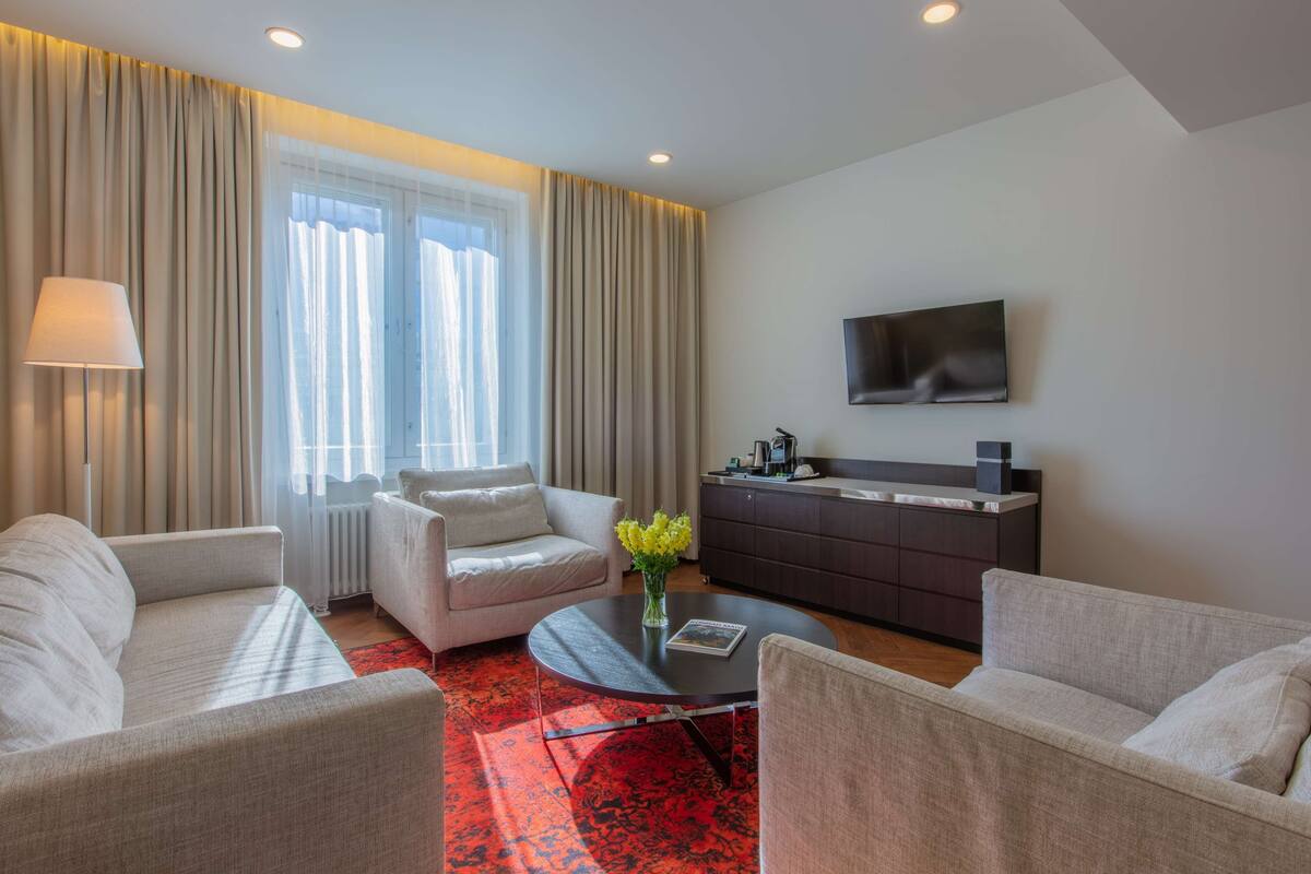 A modern hotel room with a sofa, a coffee table, a TV, and a kitchen area.