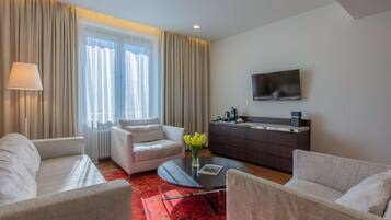 A modern hotel room with a sofa, a coffee table, a TV, and a kitchen area.