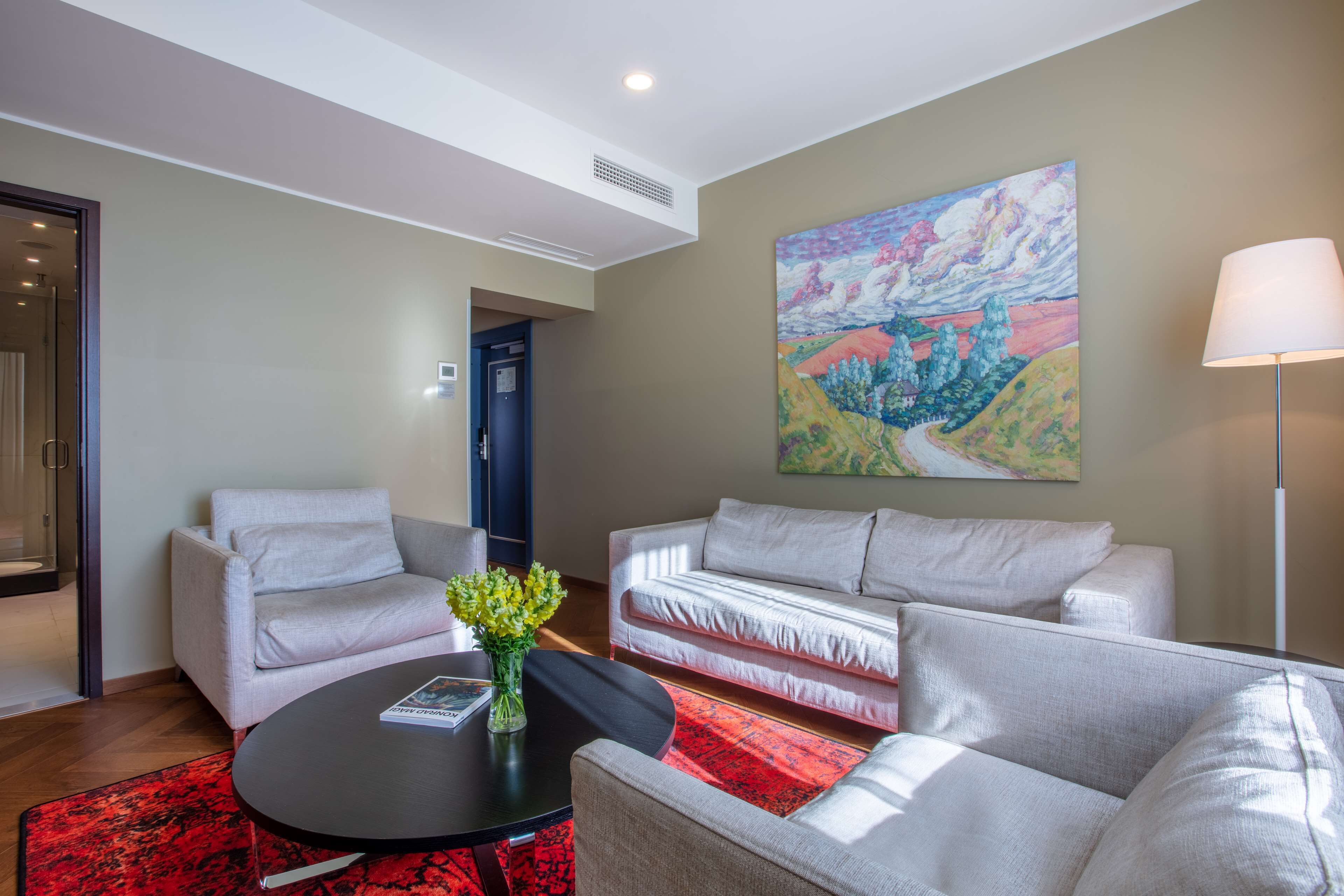A modern living room with a sofa, armchairs, a coffee table, and a painting on the wall.