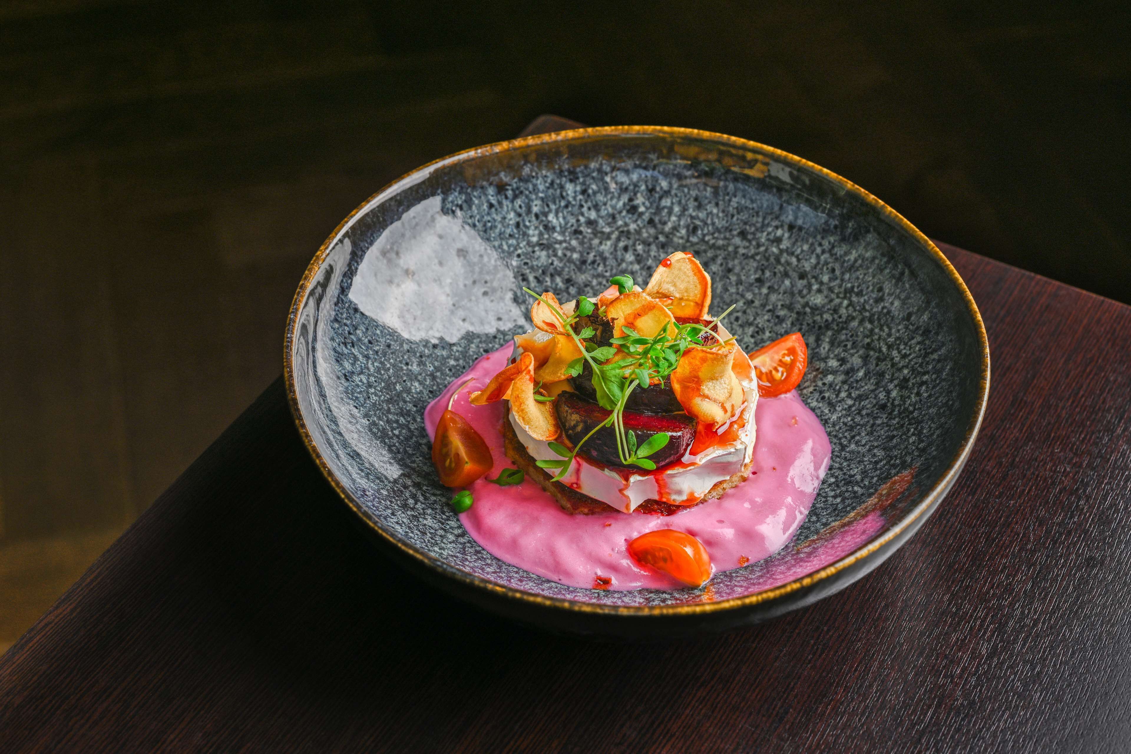 Una mesa de madera oscura con un cuenco de cerámica que contiene un plato con salsa rosada, verduras y adornos.