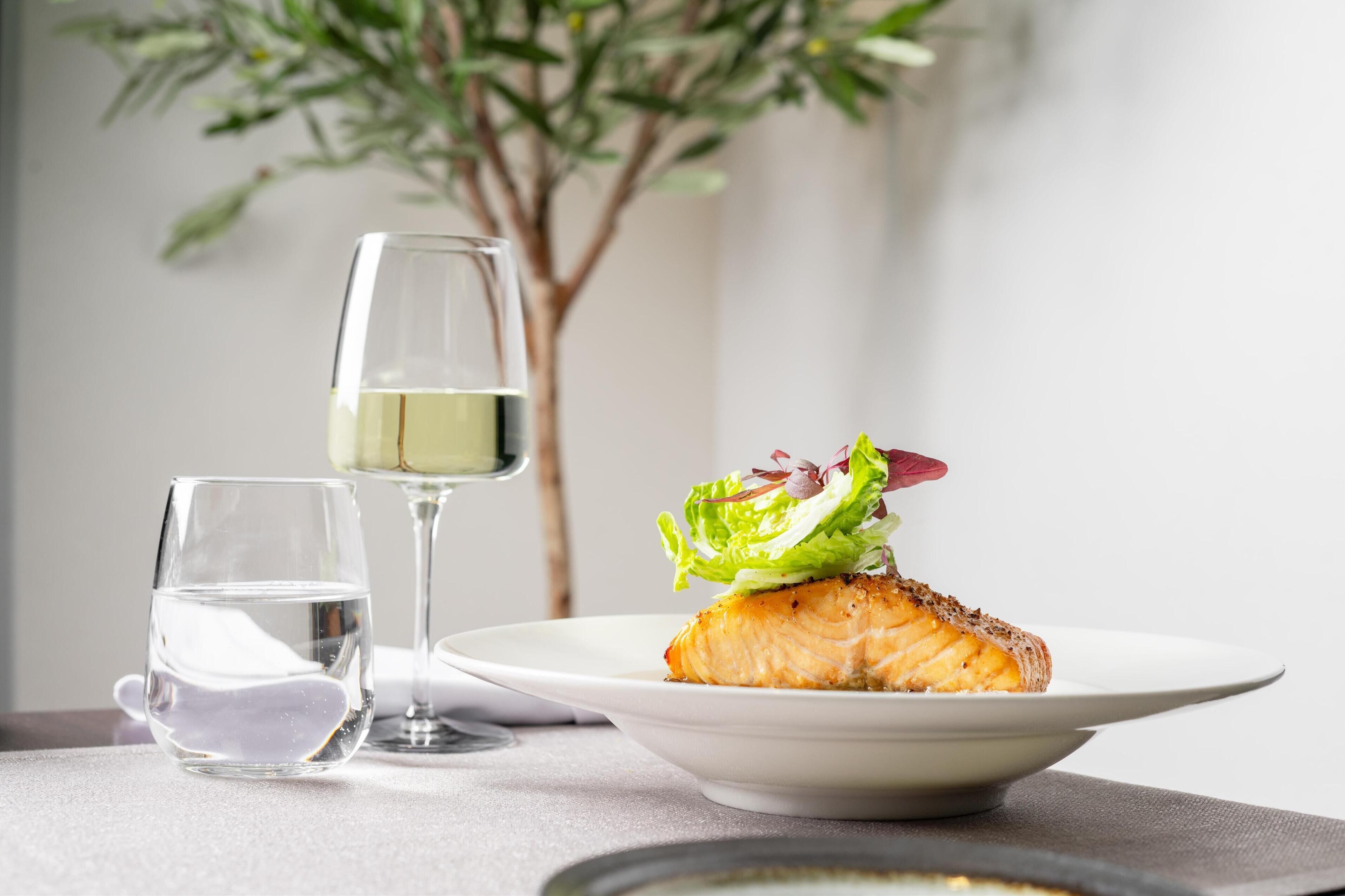 A plate with salmon and a glass of white wine on a table.