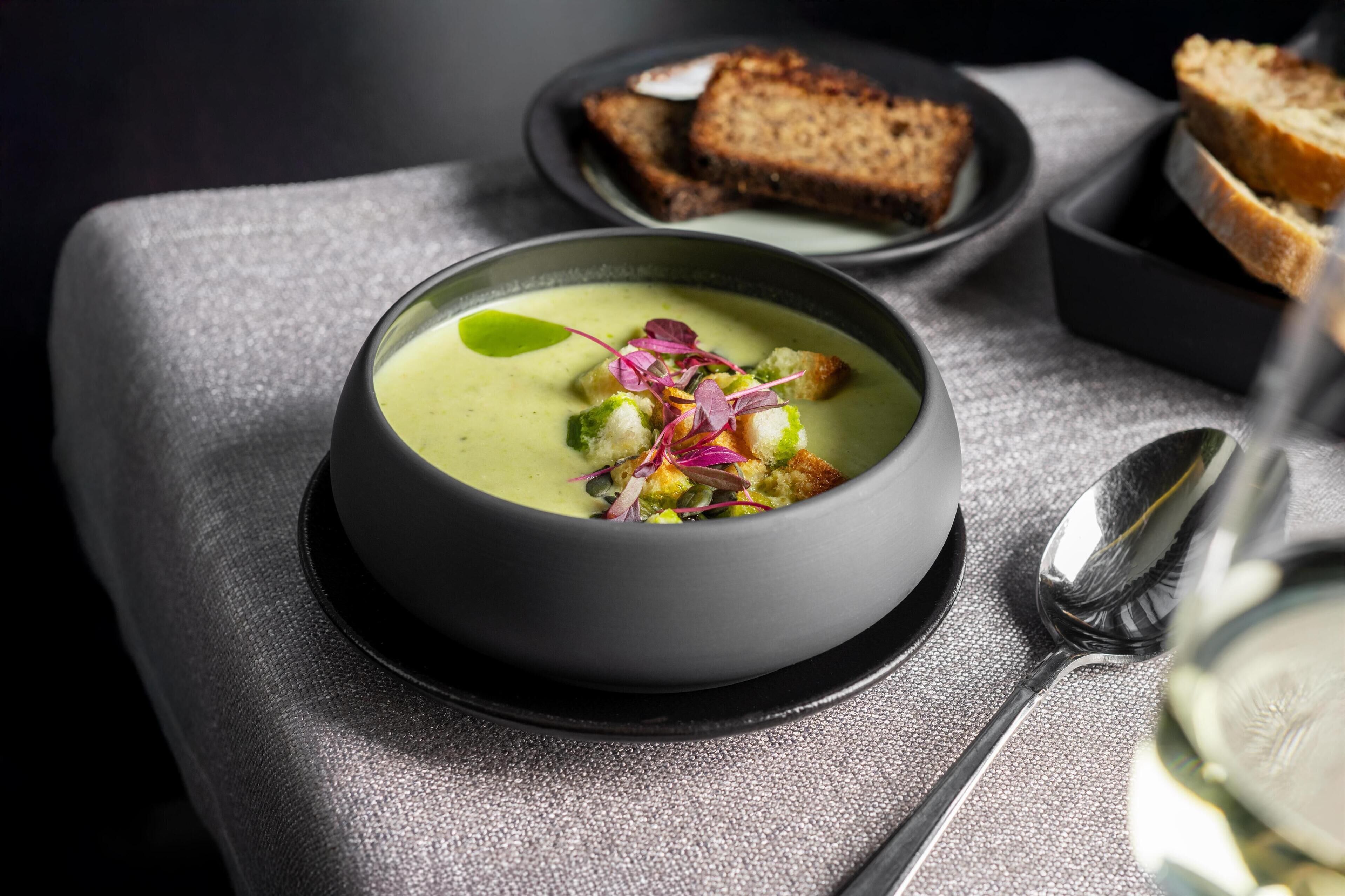 Un bol de soupe agrémenté d’une garniture, accompagné d’une cuillère et d’un verre d’eau, posés sur une table.