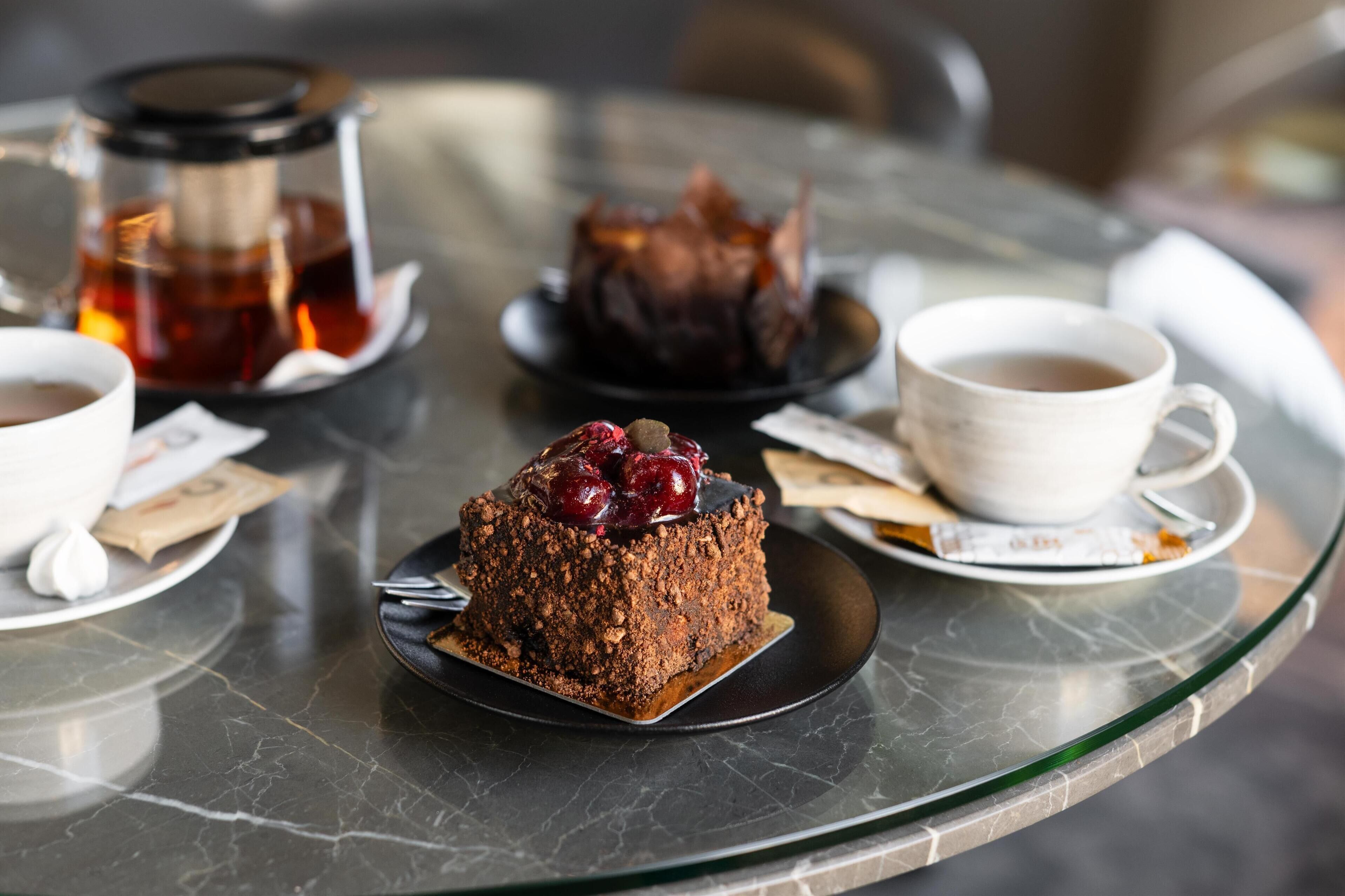 Et glastabel med en chokoladekage pyntet med kirsebær, en kaffekop og en tepotte.