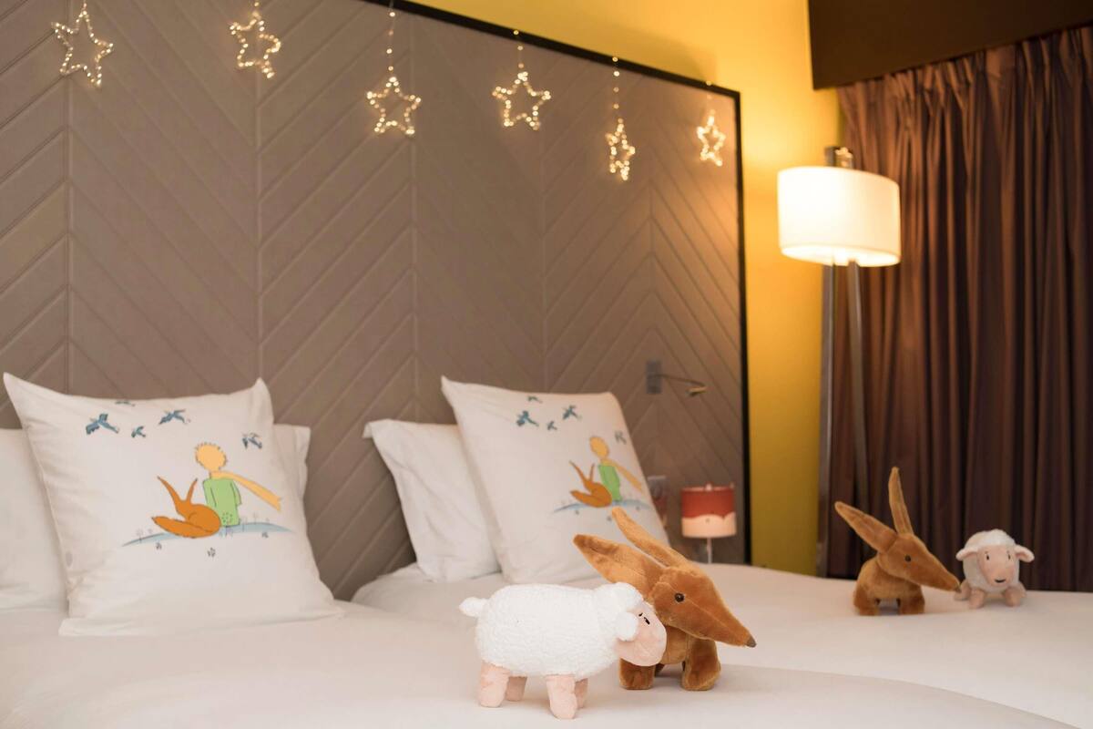 Una habitación de hotel con una cama grande, almohadones decorativos, una mesita de noche y una lámpara.