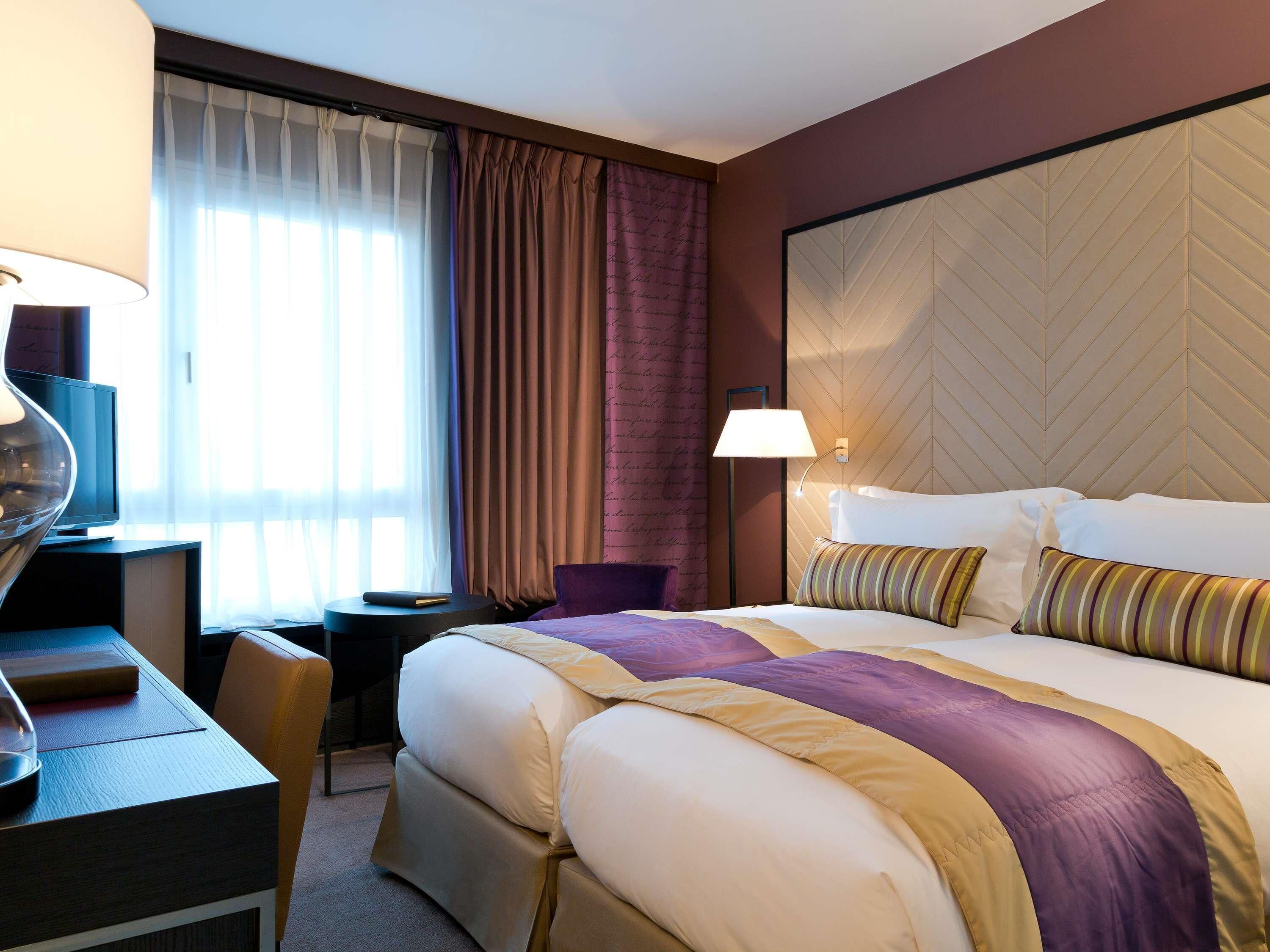 Une chambre d’hôtel avec un grand lit, un bureau avec une chaise, une télévision et une lampe.