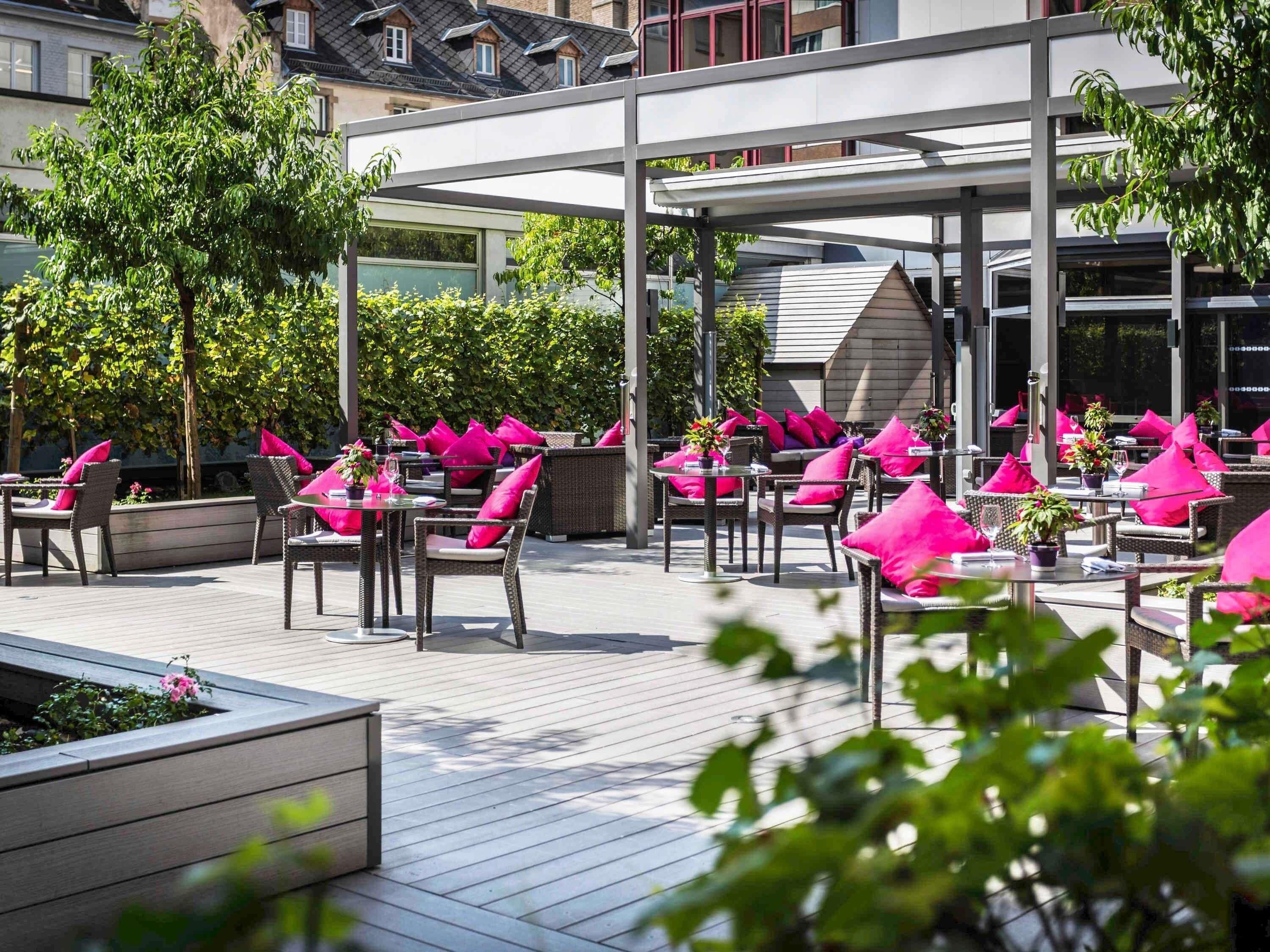 An outdoor patio with wicker furniture, pink cushions, and potted plants.