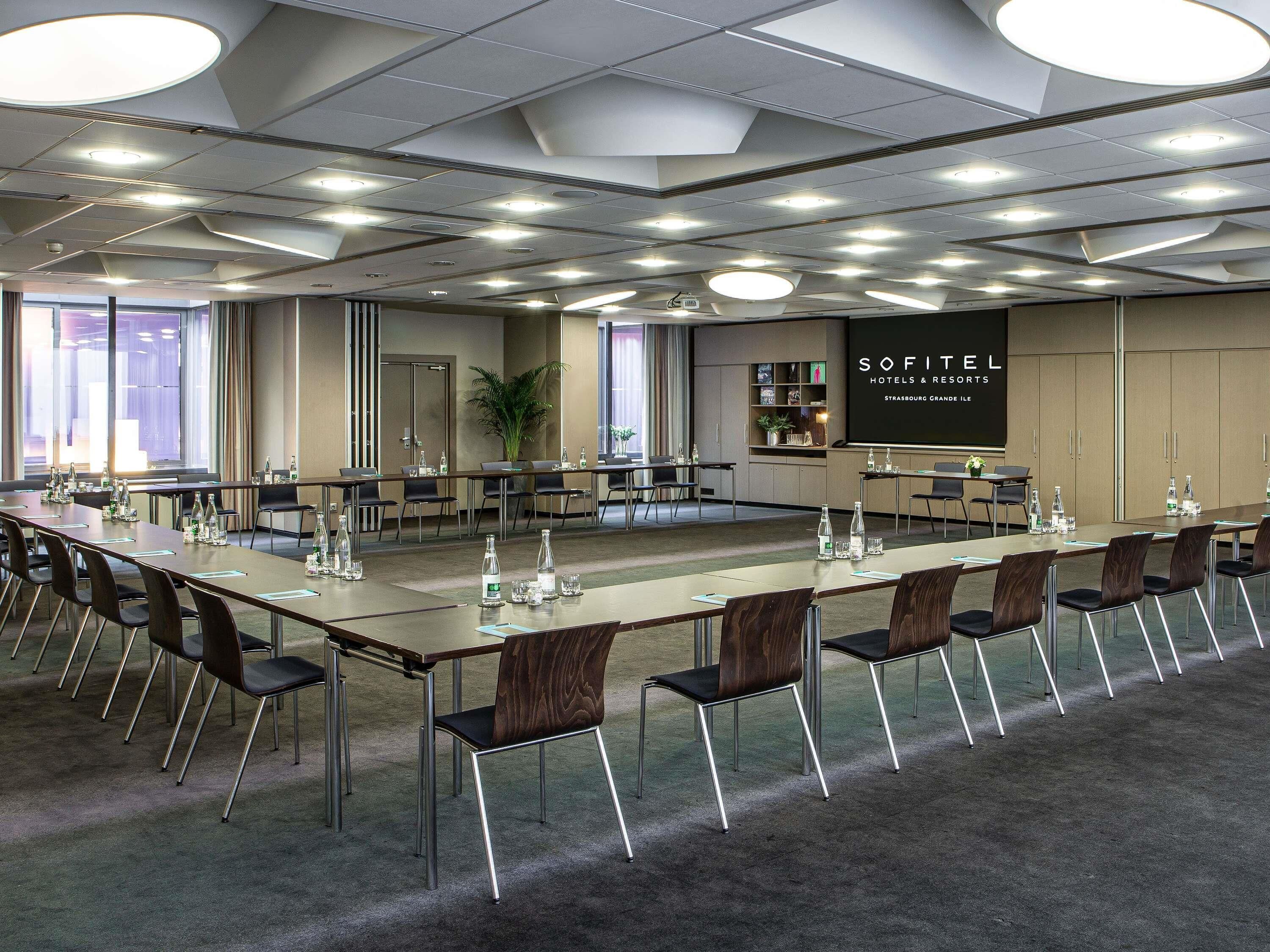 Un salón de conferencias con una larga mesa, sillas y una pantalla proyectora que muestra 'SOFITEL HOTELS & RESORTS'.