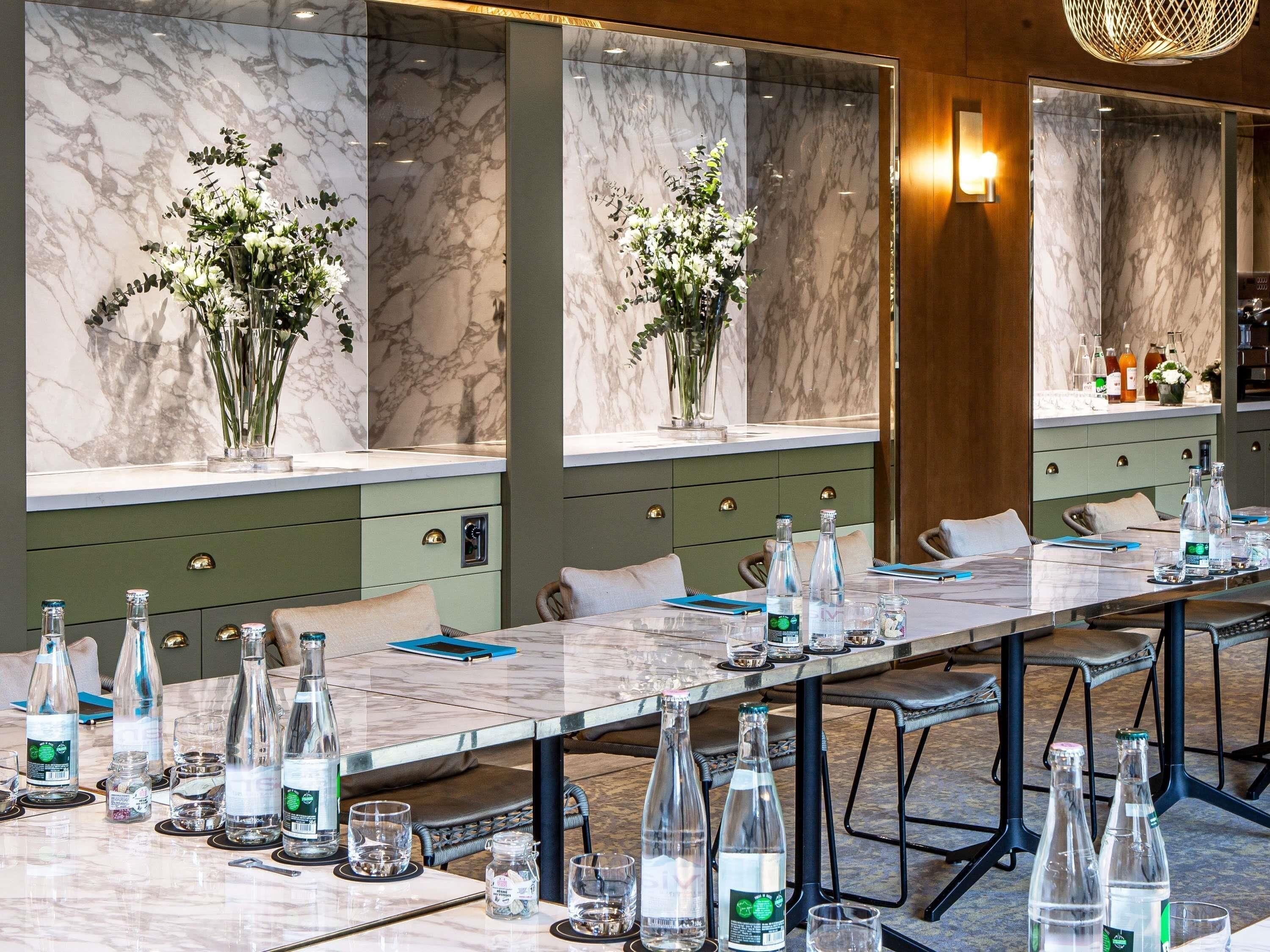 A conference room with a long table, multiple chairs, and vases with flowers.