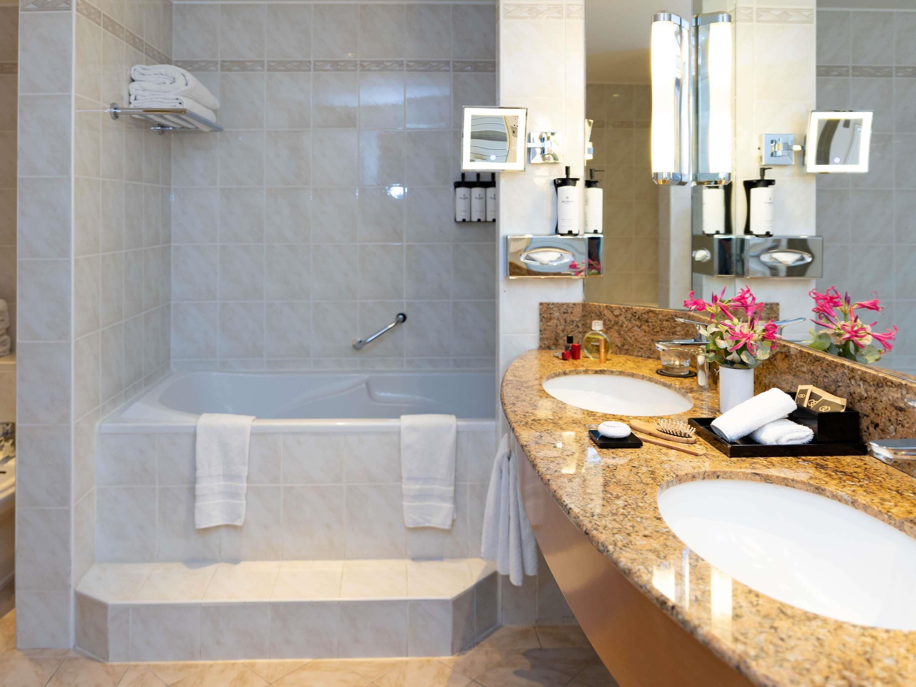 A modern bathroom with a bathtub, two sinks, and a vanity area.