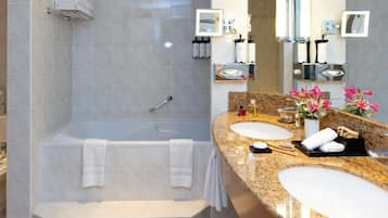A modern bathroom with a bathtub, two sinks, and a vanity area.