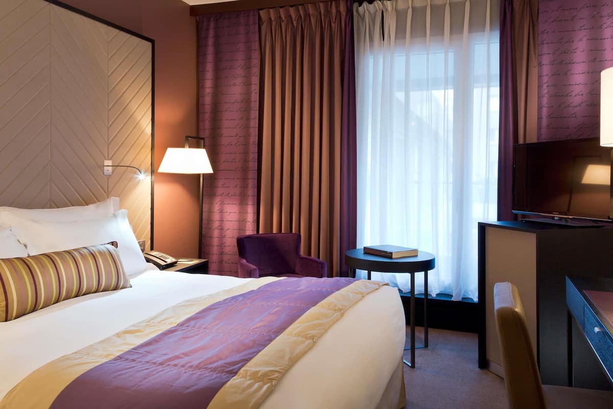Una habitación de hotel con una cama grande, un escritorio, una silla, un televisor y cortinas.