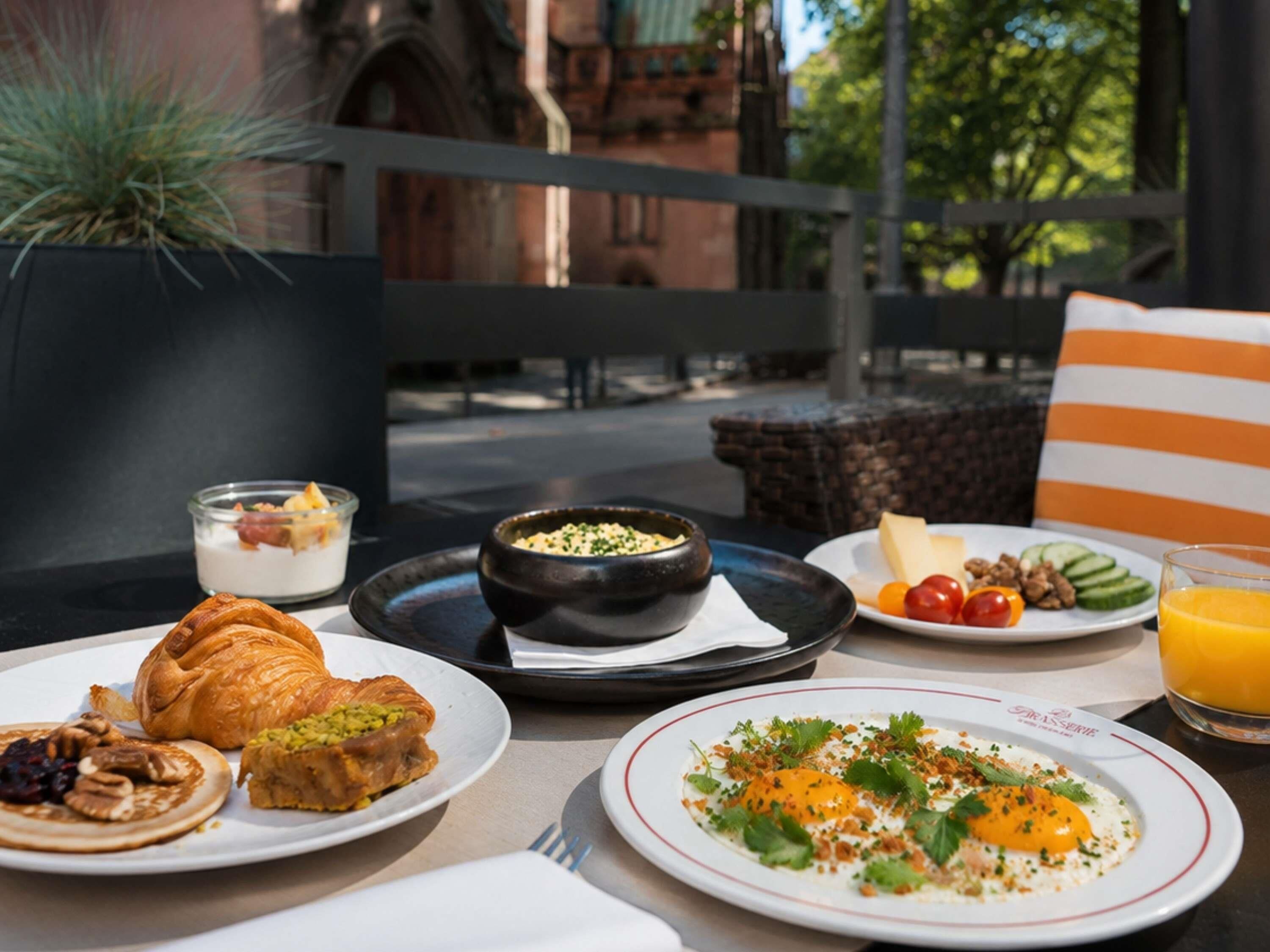 A breakfast setting with croissants, a bowl of cereal, a plate with cheese and tomatoes, and a glass of orange juice.
