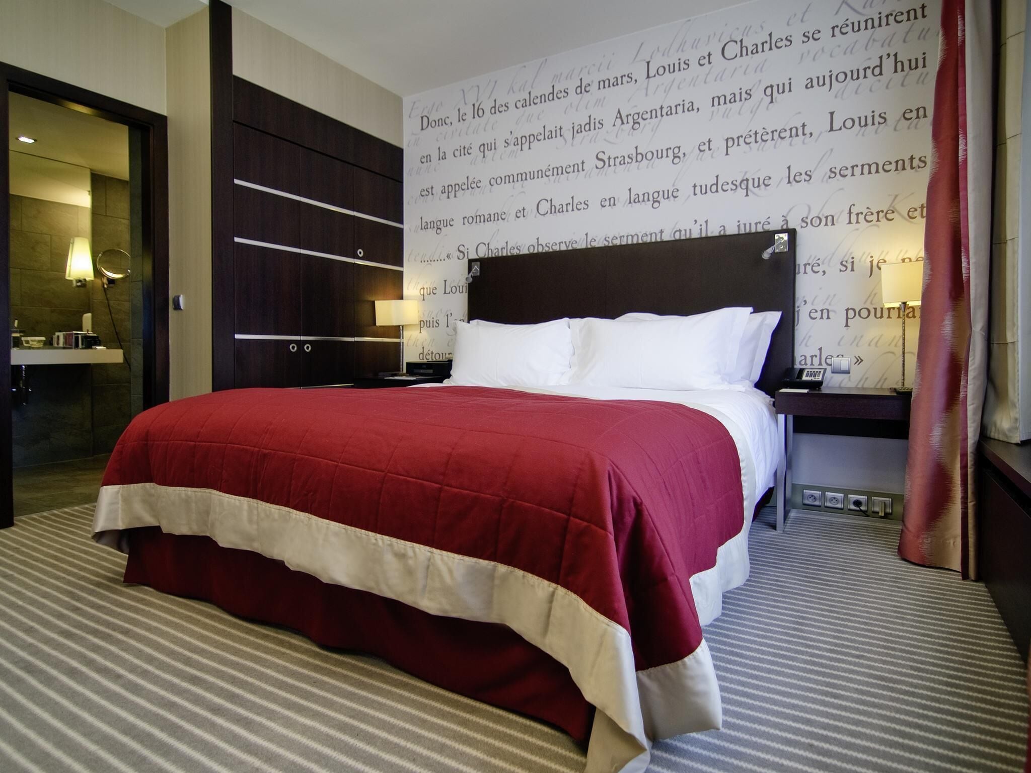 A hotel room with a large bed, a nightstand, a lamp, and a wall with text.