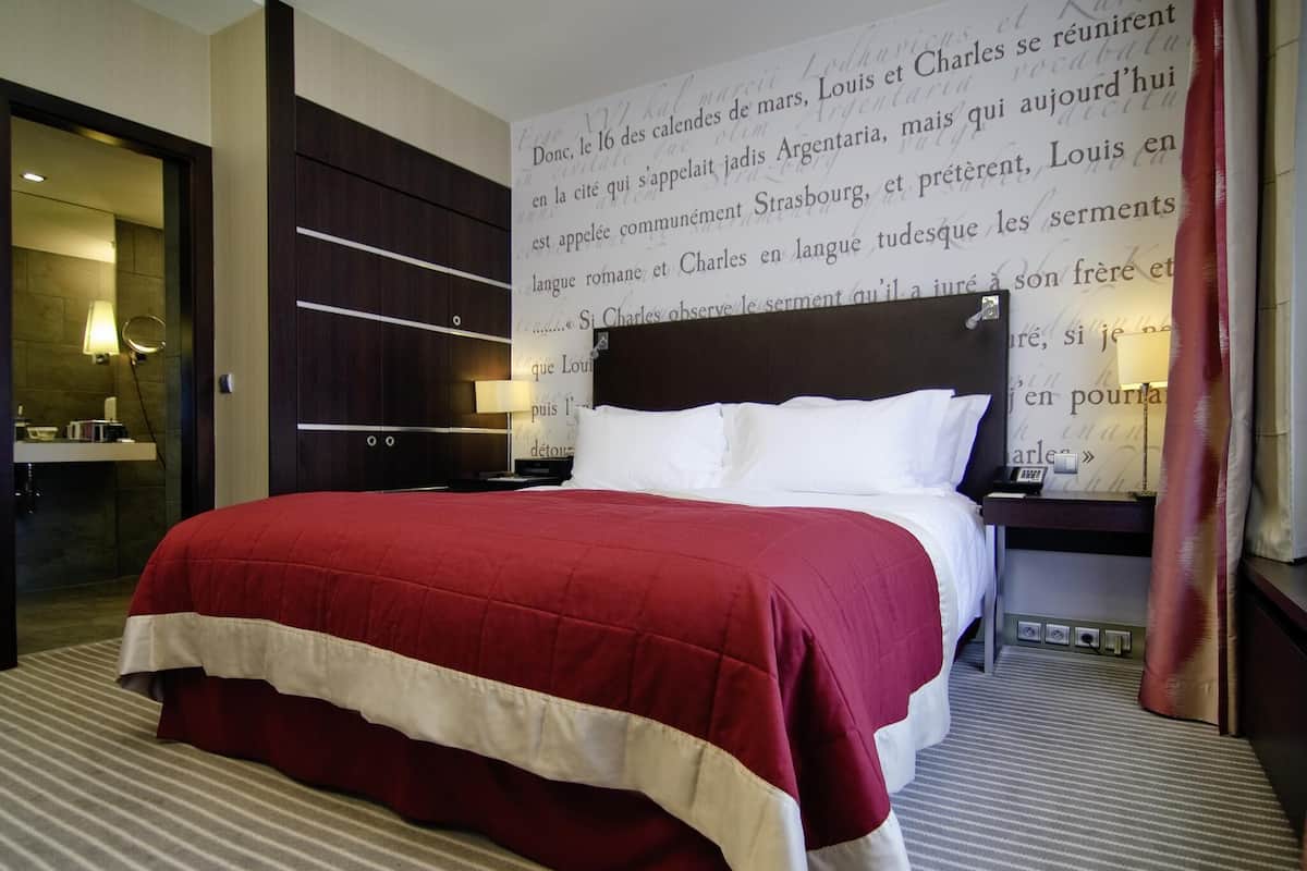 A hotel room with a large bed, a nightstand, a lamp, and a wall with text.