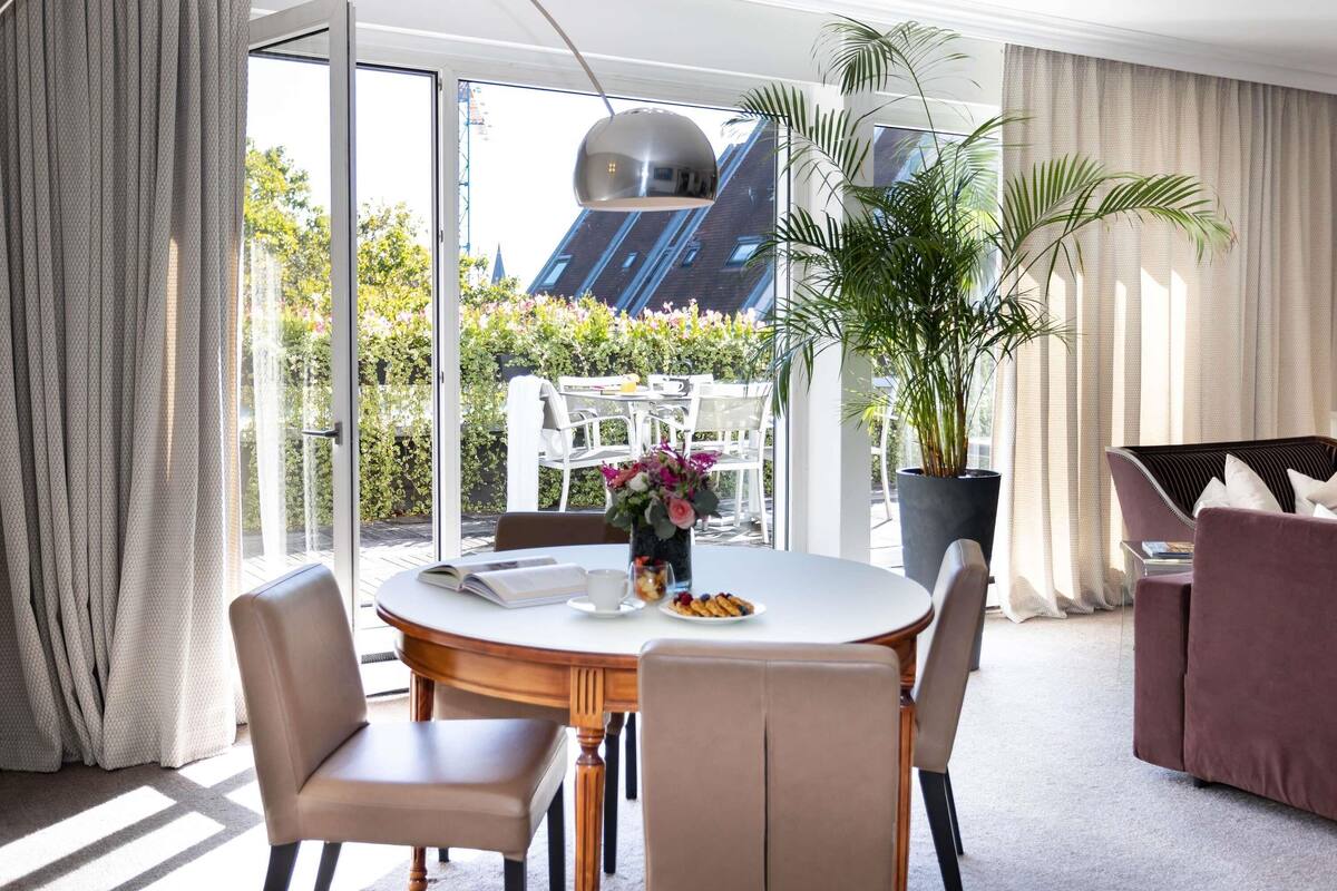 Un comedor moderno con una mesa redonda, sillas, una planta en maceta y vistas al exterior.