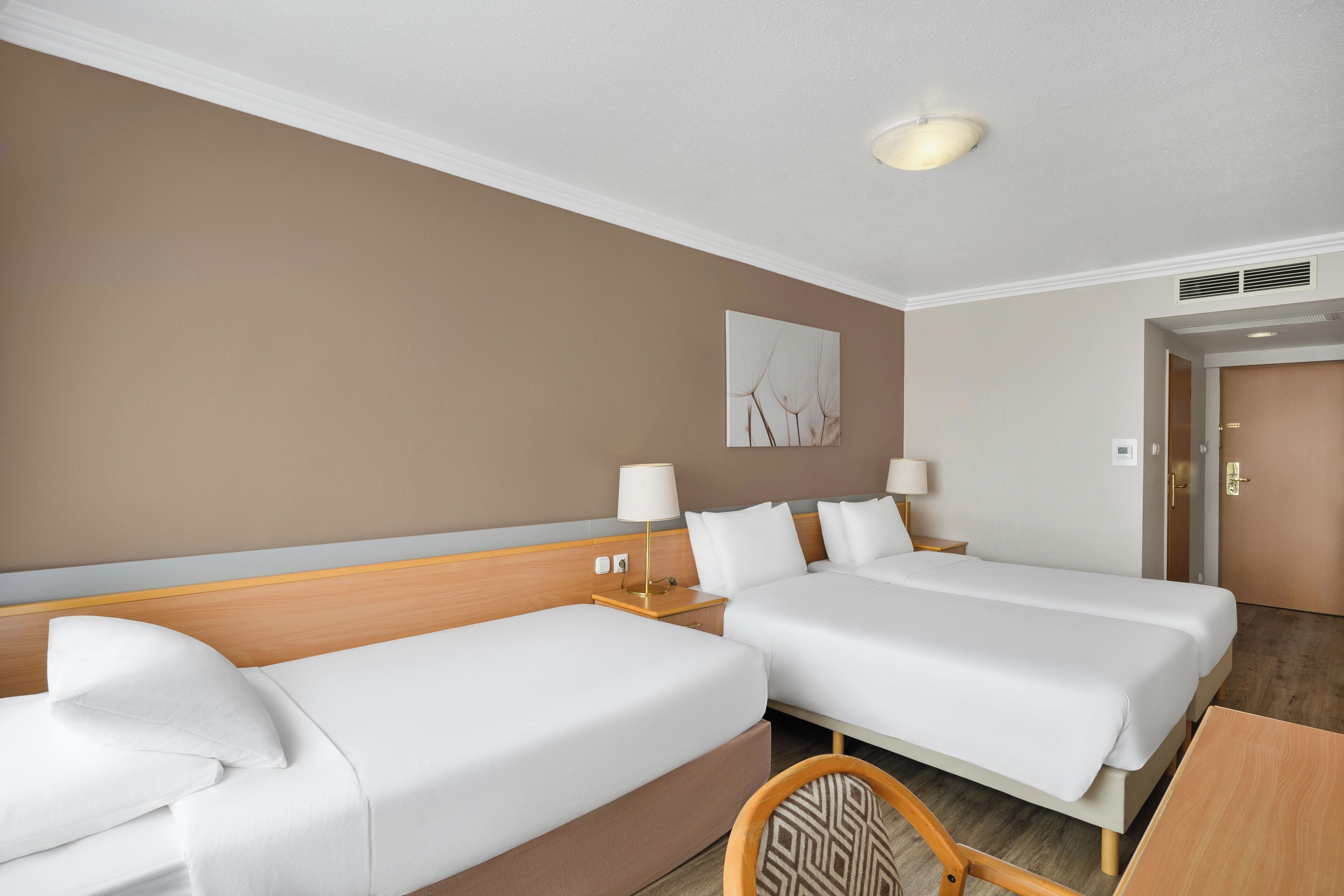 A hotel room with two beds, a wooden headboard, a wall-mounted artwork, and a door with a handle.
