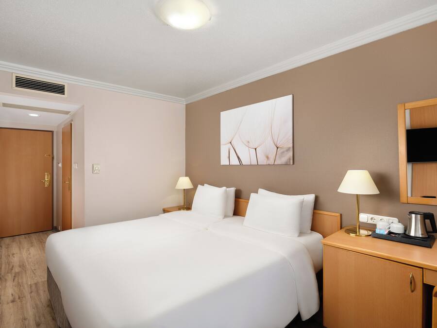 Una habitación de hotel con una cama grande, mesitas de noche, un escritorio y un espejo.
