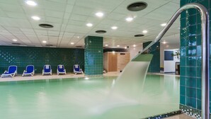 Piscina con sillas azules, pared de vidrio y una escalera.