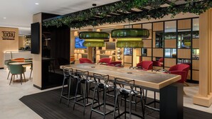 Un moderno bar bistró con una larga mesa de madera, sillas rojas y lámparas colgantes verdes.