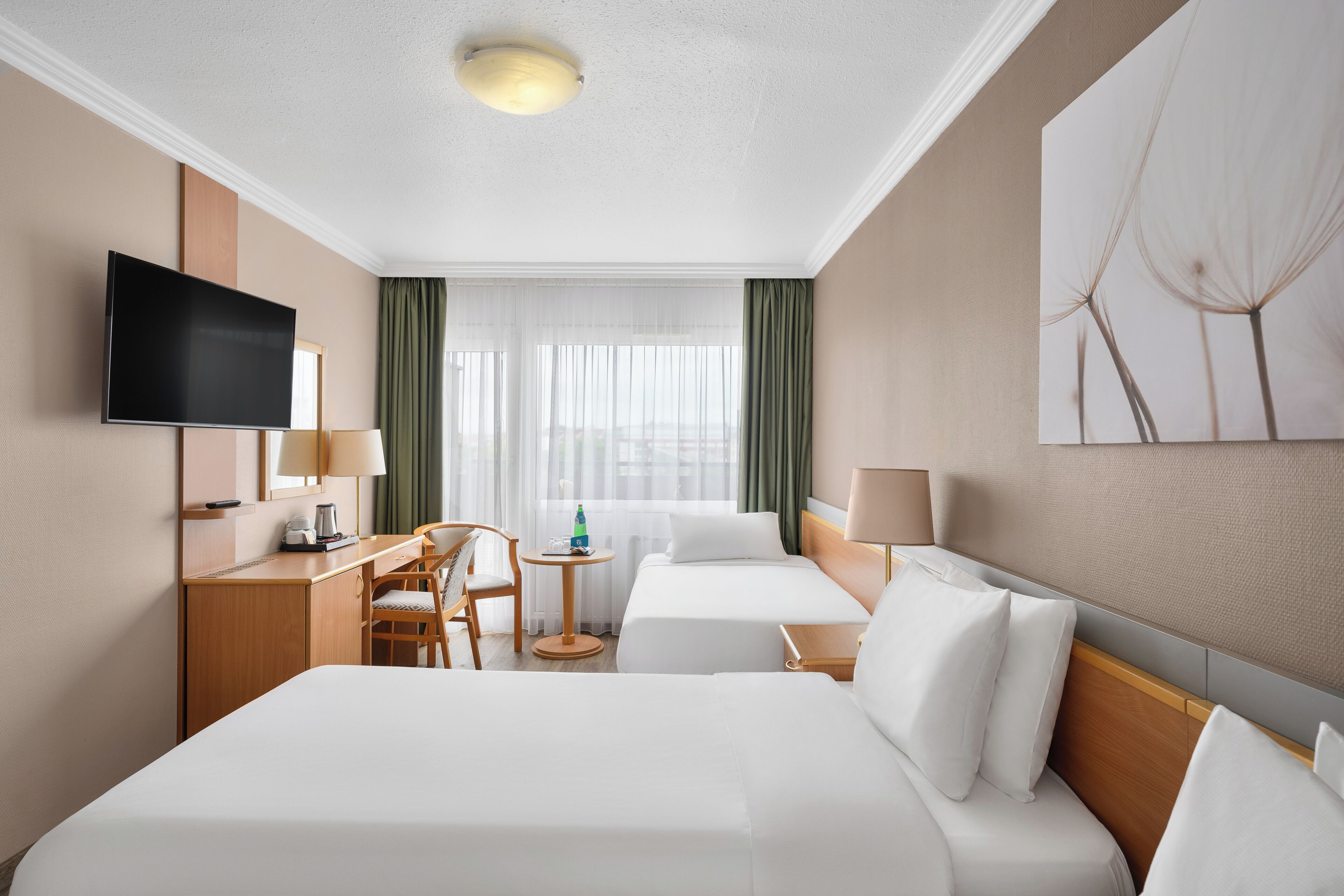 Habitación de hotel con cama, escritorio, silla, televisor y ventana con cortinas.