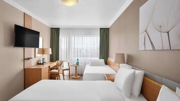 Habitación de hotel con cama, escritorio, silla, televisor y ventana con cortinas.