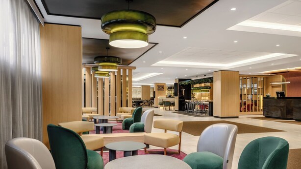 Un moderno vestíbulo de hotel con áreas de estar, una recepción y una zona de bar y lounge.