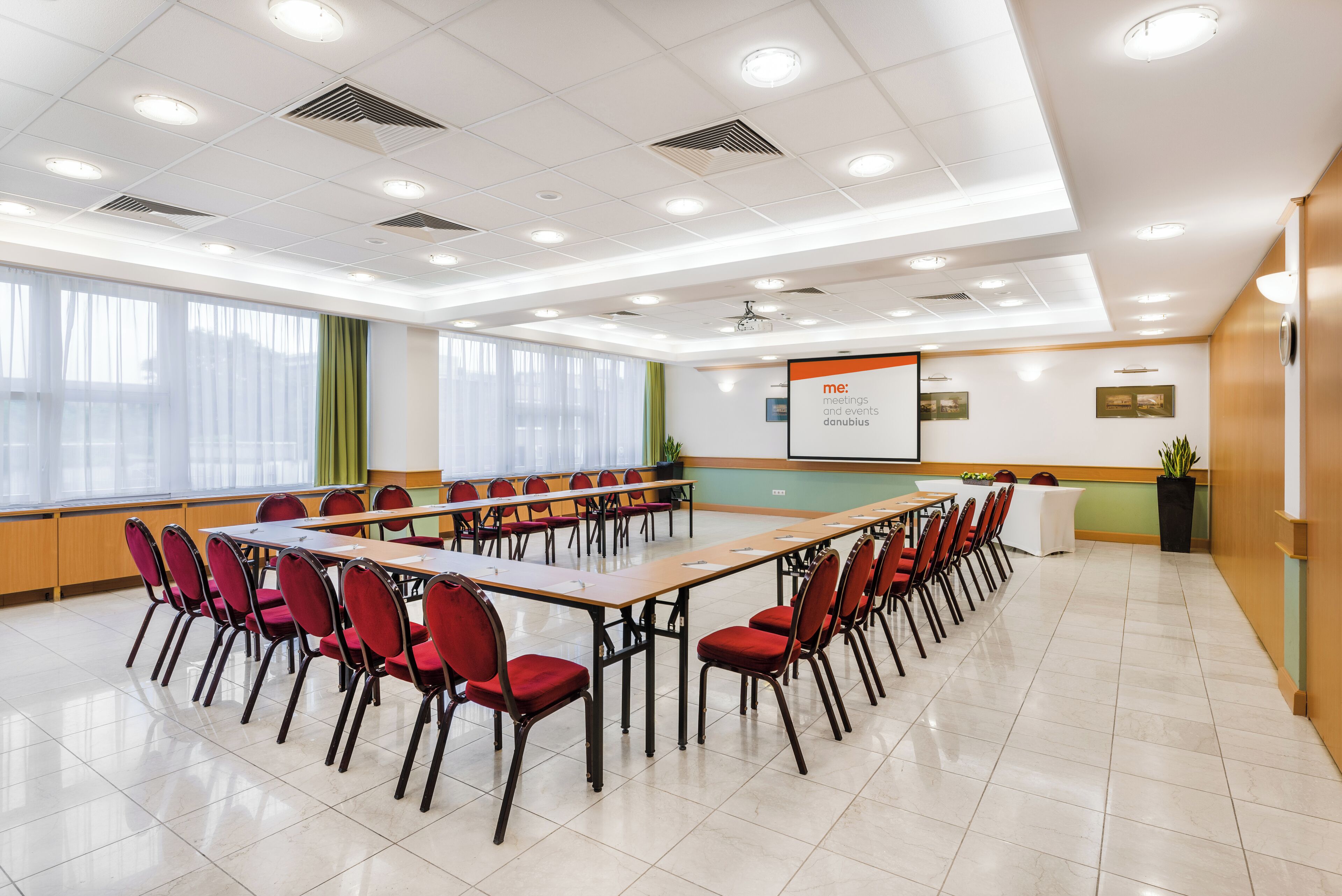 A conference room with a long table, red chairs, a projector screen, and a whiteboard.