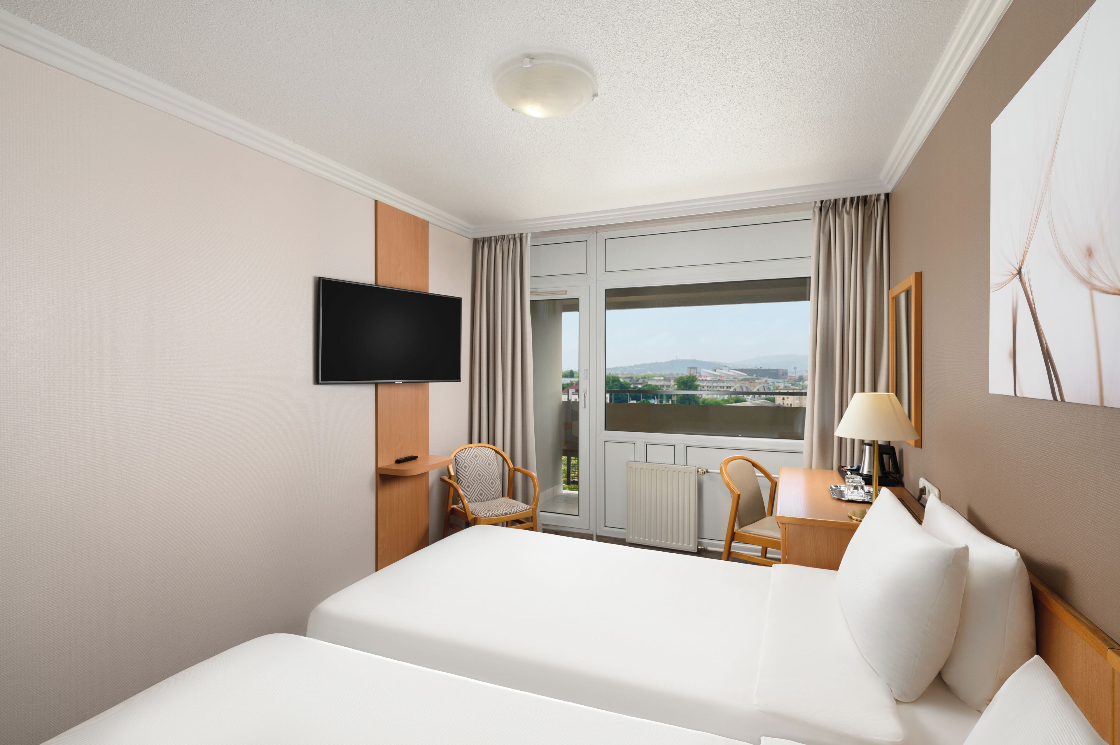 A hotel room with a bed, a TV, a desk, a chair, and a window with curtains.