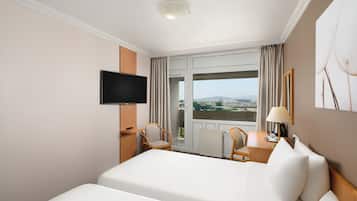 A hotel room with a bed, a TV, a desk, a chair, and a window with curtains.