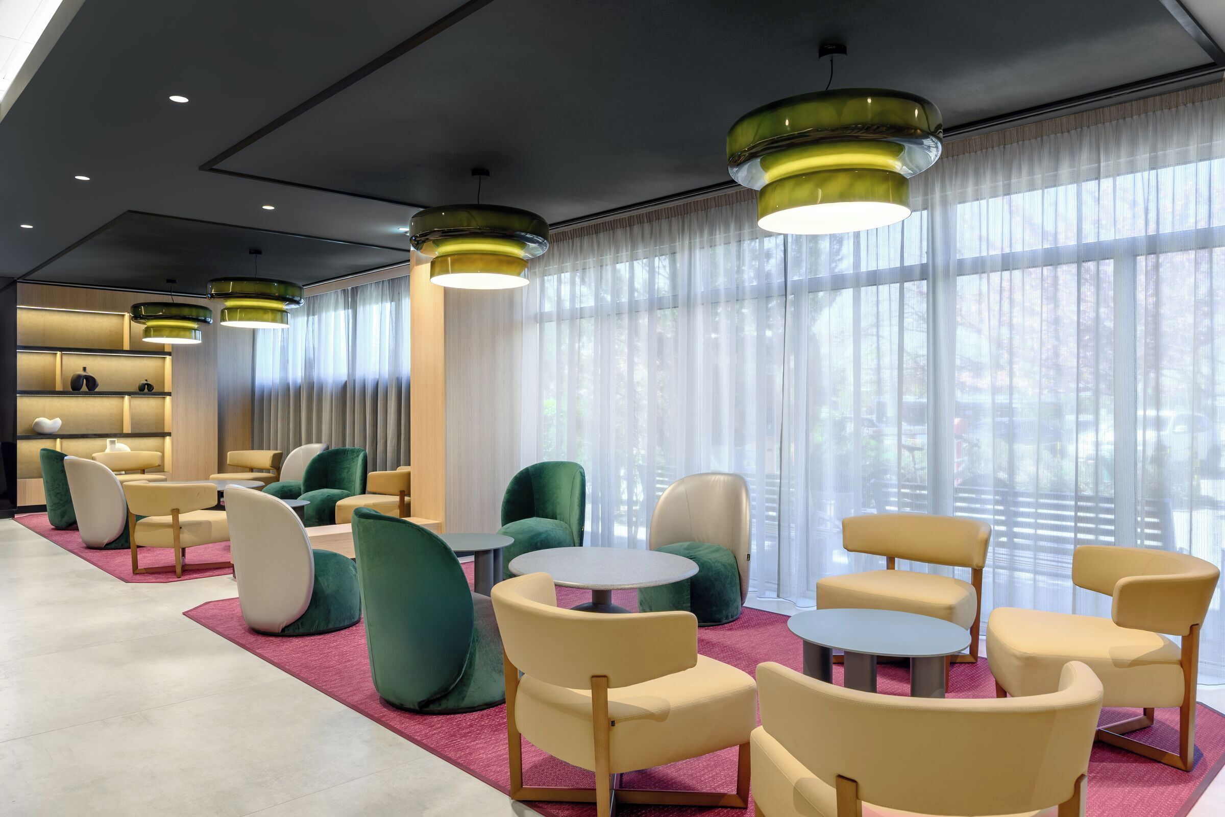 A modern hotel lobby with green and beige chairs, round tables, and pendant lighting.