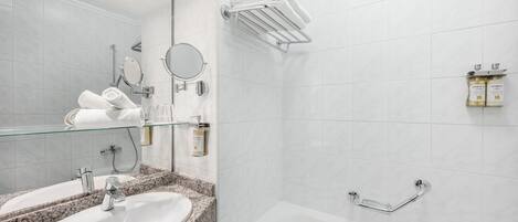 Un baño moderno con lavamanos de encimera de granito, espejo con puerta de cristal, cabezal de ducha de mano y bañera blanca con barra de apoyo cromada.