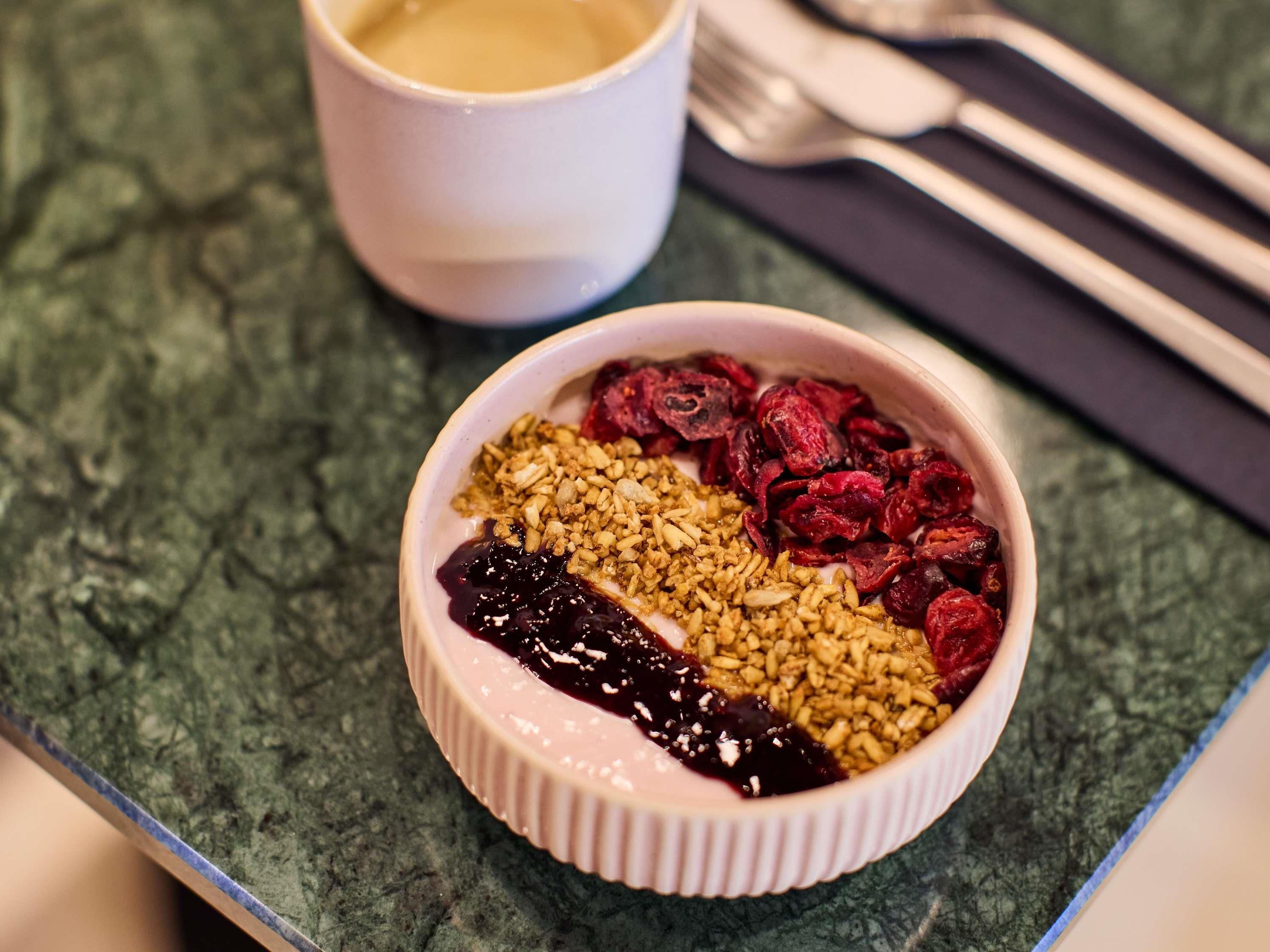 A dessert bowl with granola, dried berries, and a dark fruit compote on a textured surface.