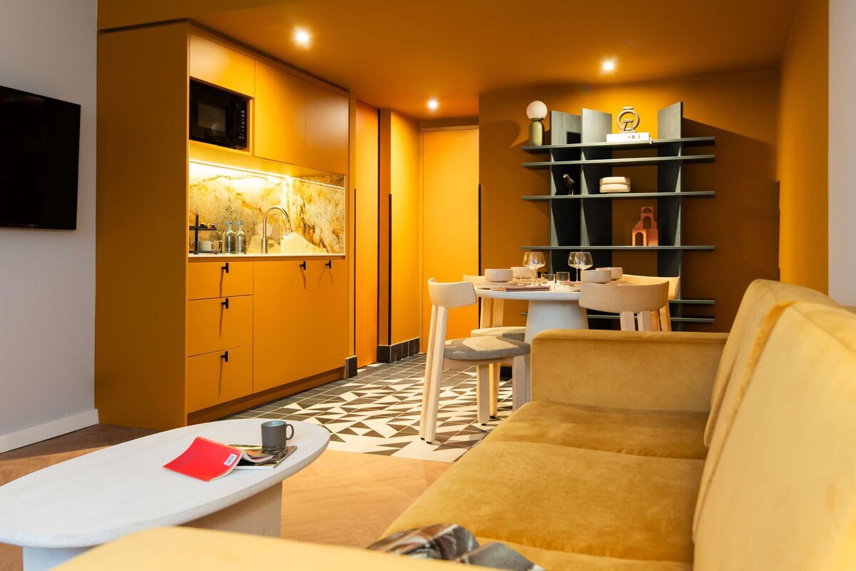 Un salon moderne comprenant un canapé, une table basse, un coin repas avec une table et des chaises, et un coin cuisine avec des placards et un four à micro-ondes.