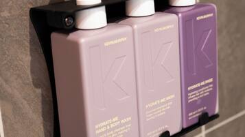 A set of three hand and body wash bottles with pumps, labeled 'Kevin Murphy', on a tiled wall.