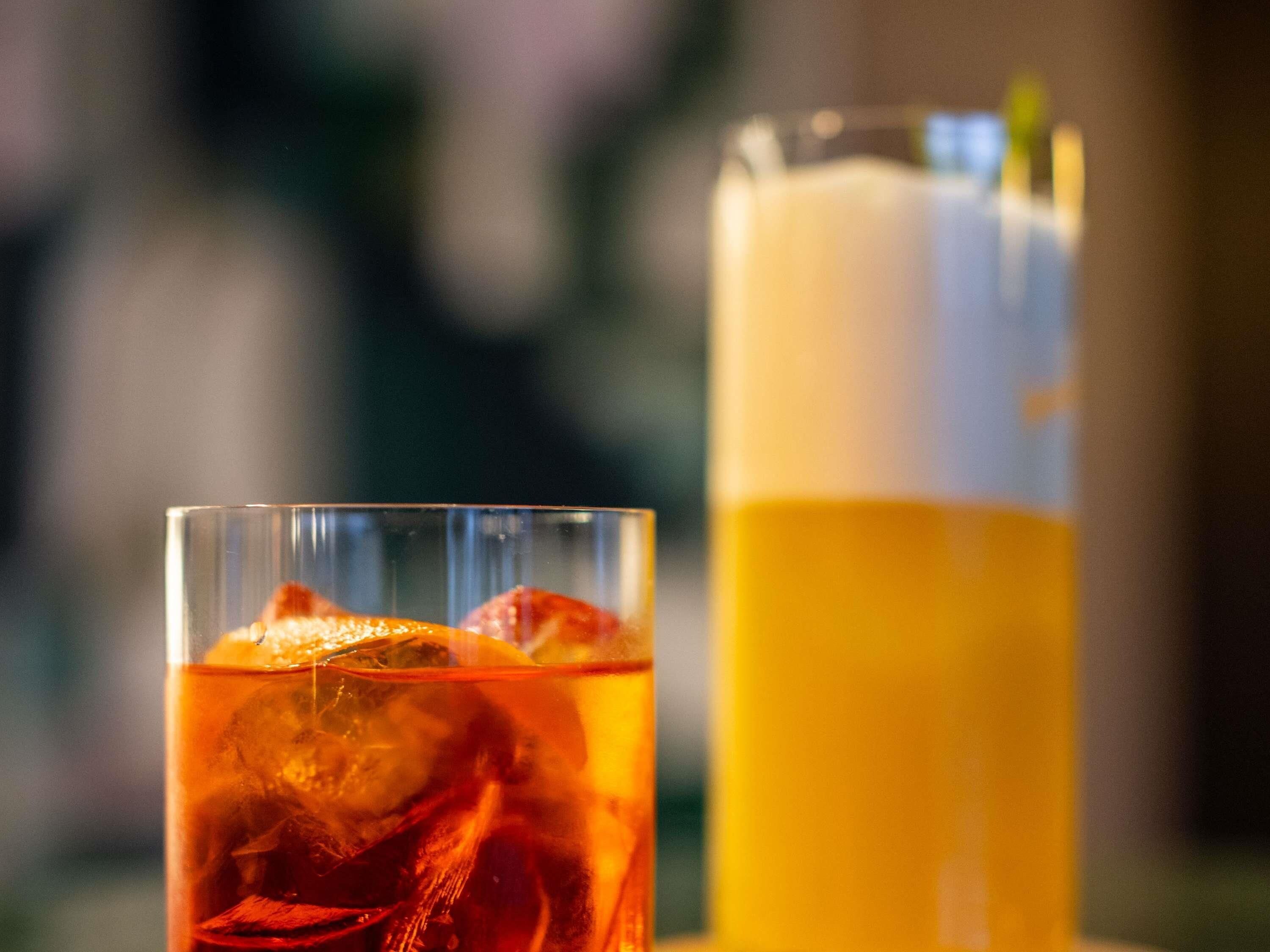 Twee glazen drankjes, één met een rode vloeistof en de ander met een gele vloeistof, allebei met ijsblokjes.