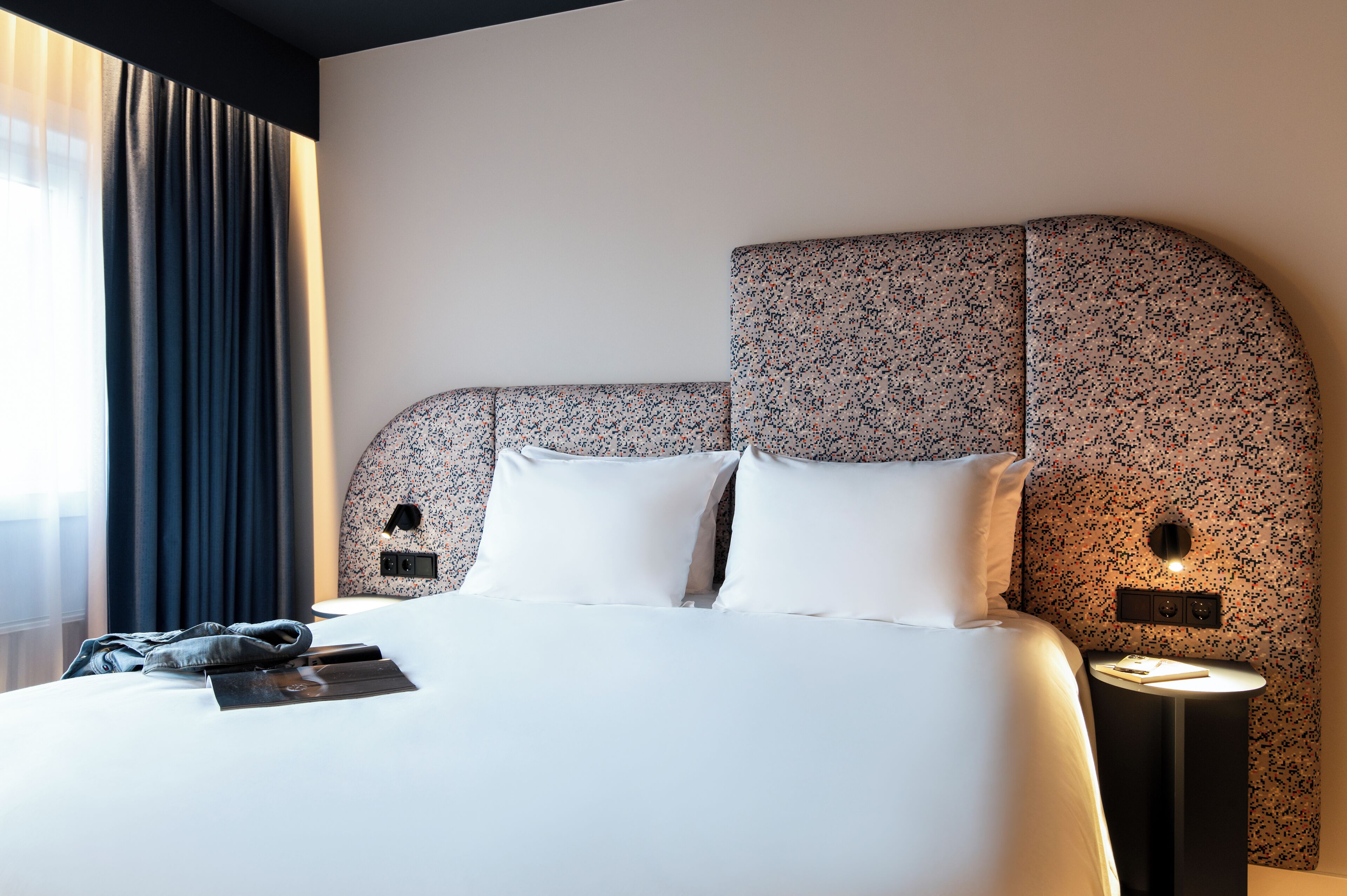 Una habitación de hotel con una cama grande, una mesita de noche y una lámpara de pared.