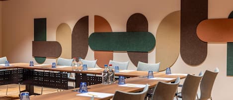 Una sala conferenze con un lungo tavolo, sedie, bottiglie d'acqua e una parete con forme astratte.