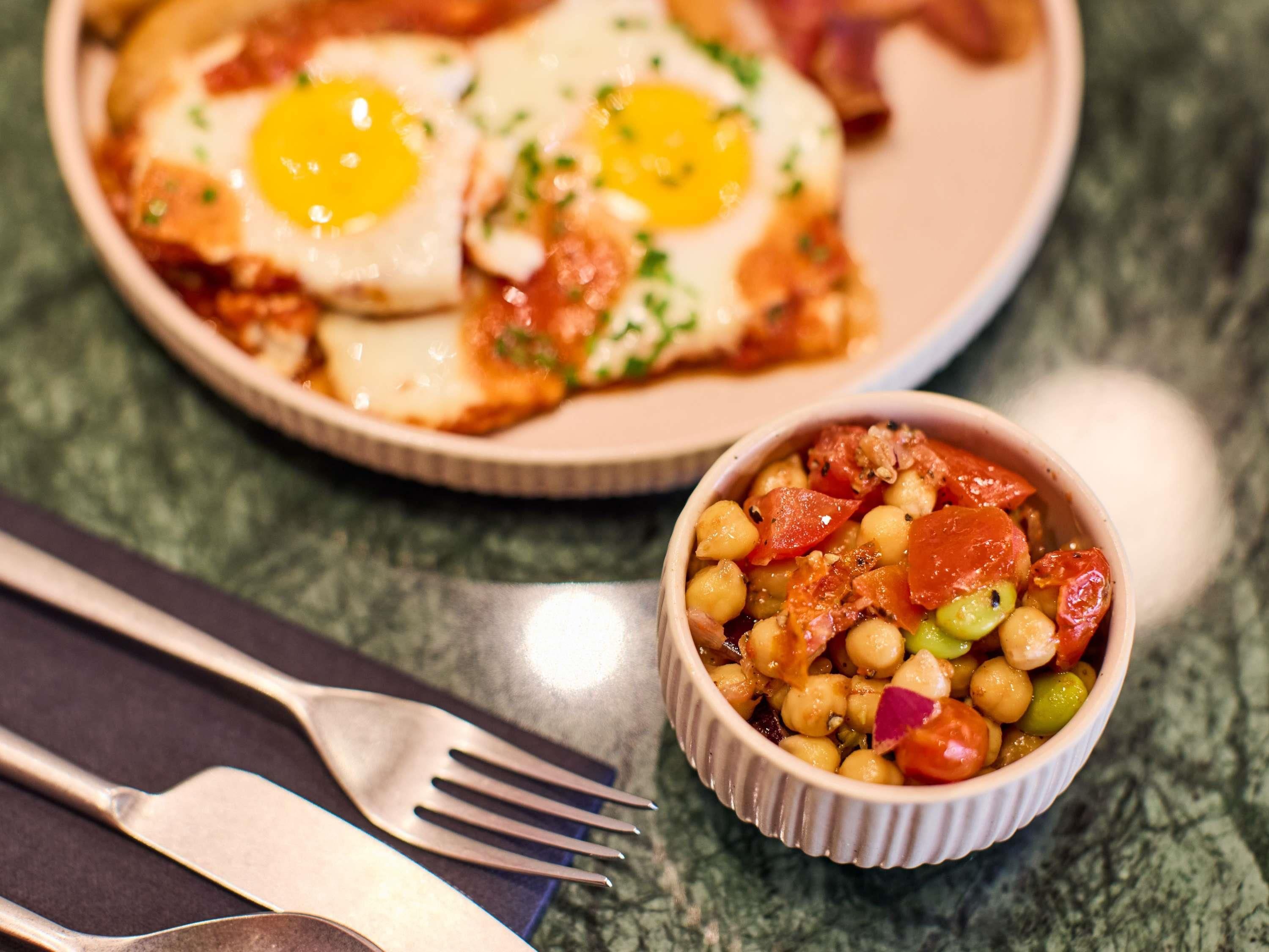 Une assiette avec deux œufs frits et un bol de pois chiches aux légumes.