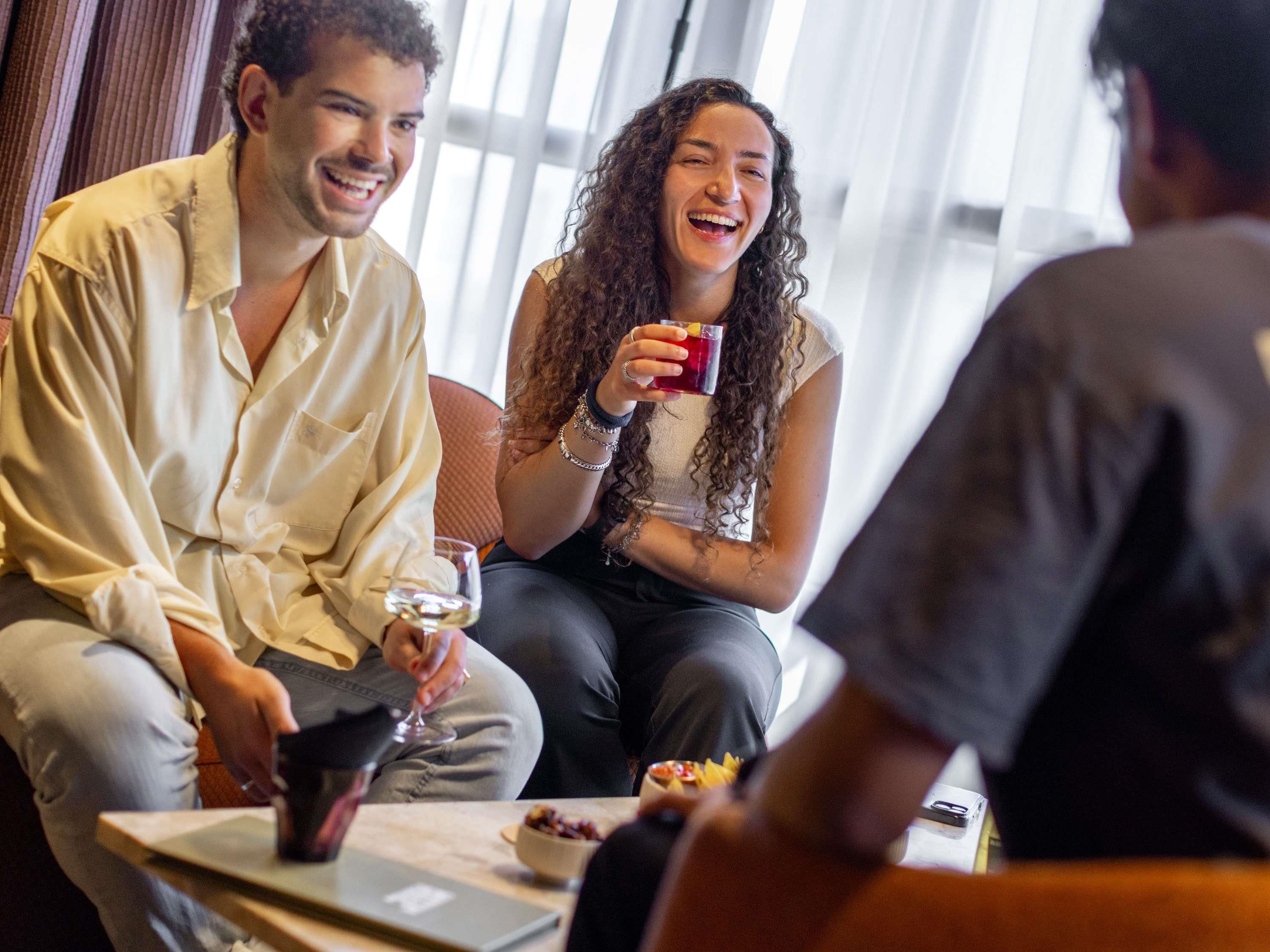 A group of people seated at a table with a laptop, a glass of wine, and a bowl of food.