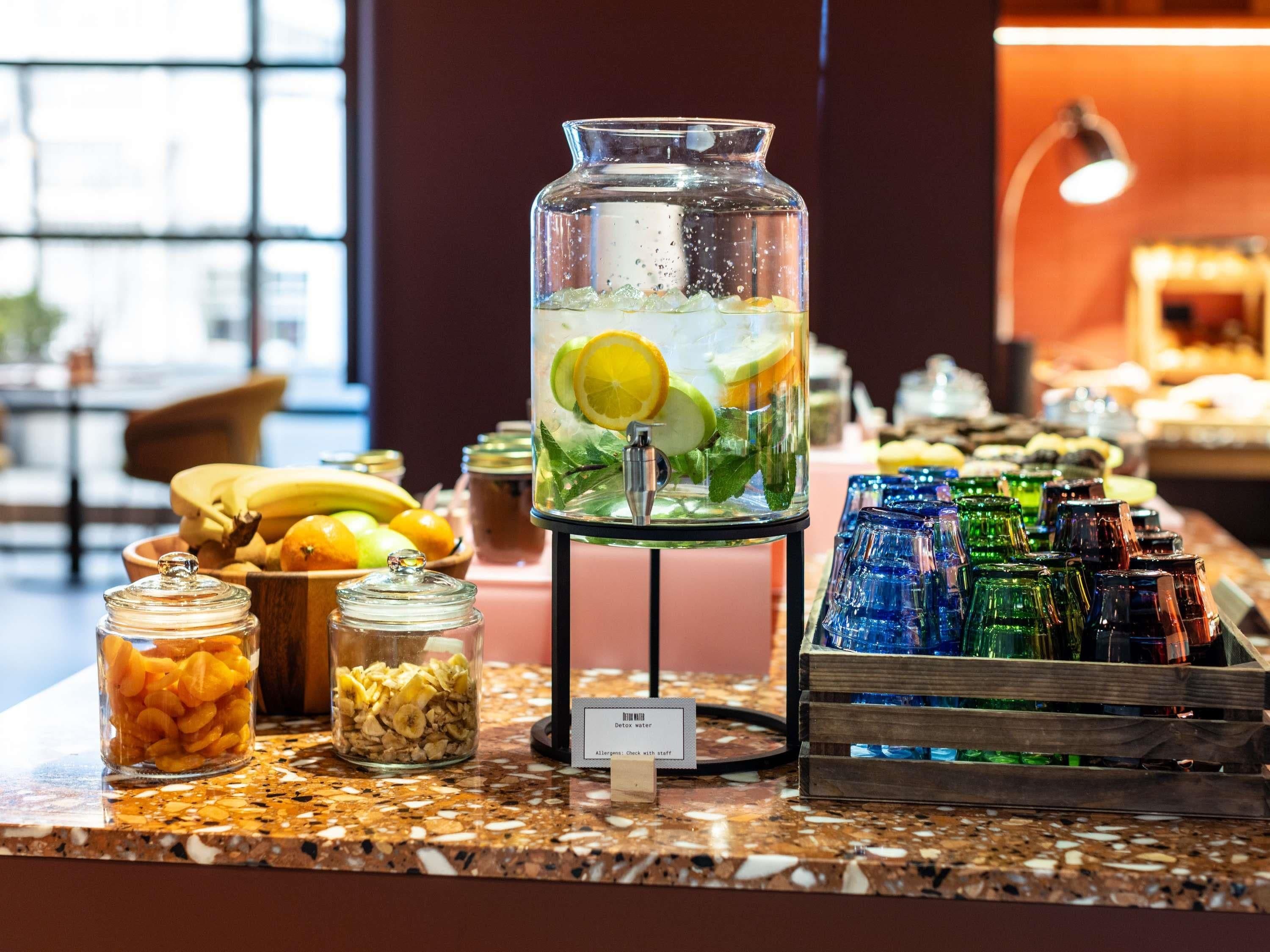 A buffet setup with a water dispenser, fruit bowls, and a variety of glassware.