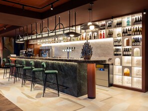 Zona de bar con mostrador de mármol, taburetes verdes y una vitrina para vinos.
