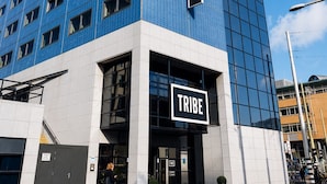 A modern building with a prominent 'TRIBE' sign, featuring a glass facade and a white base.