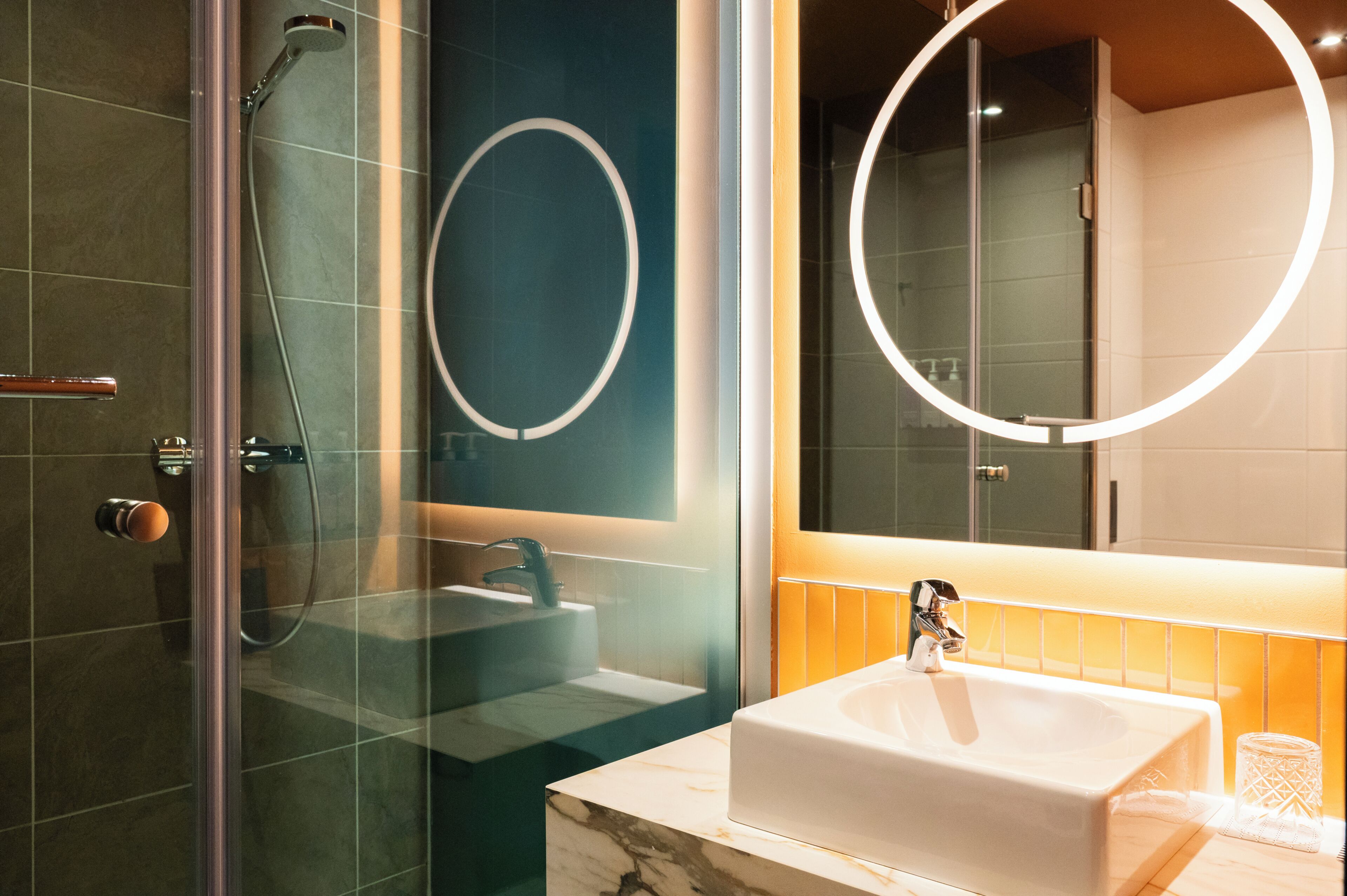 A modern bathroom with a glass-enclosed shower, a white sink, and a large mirror with a circular frame.