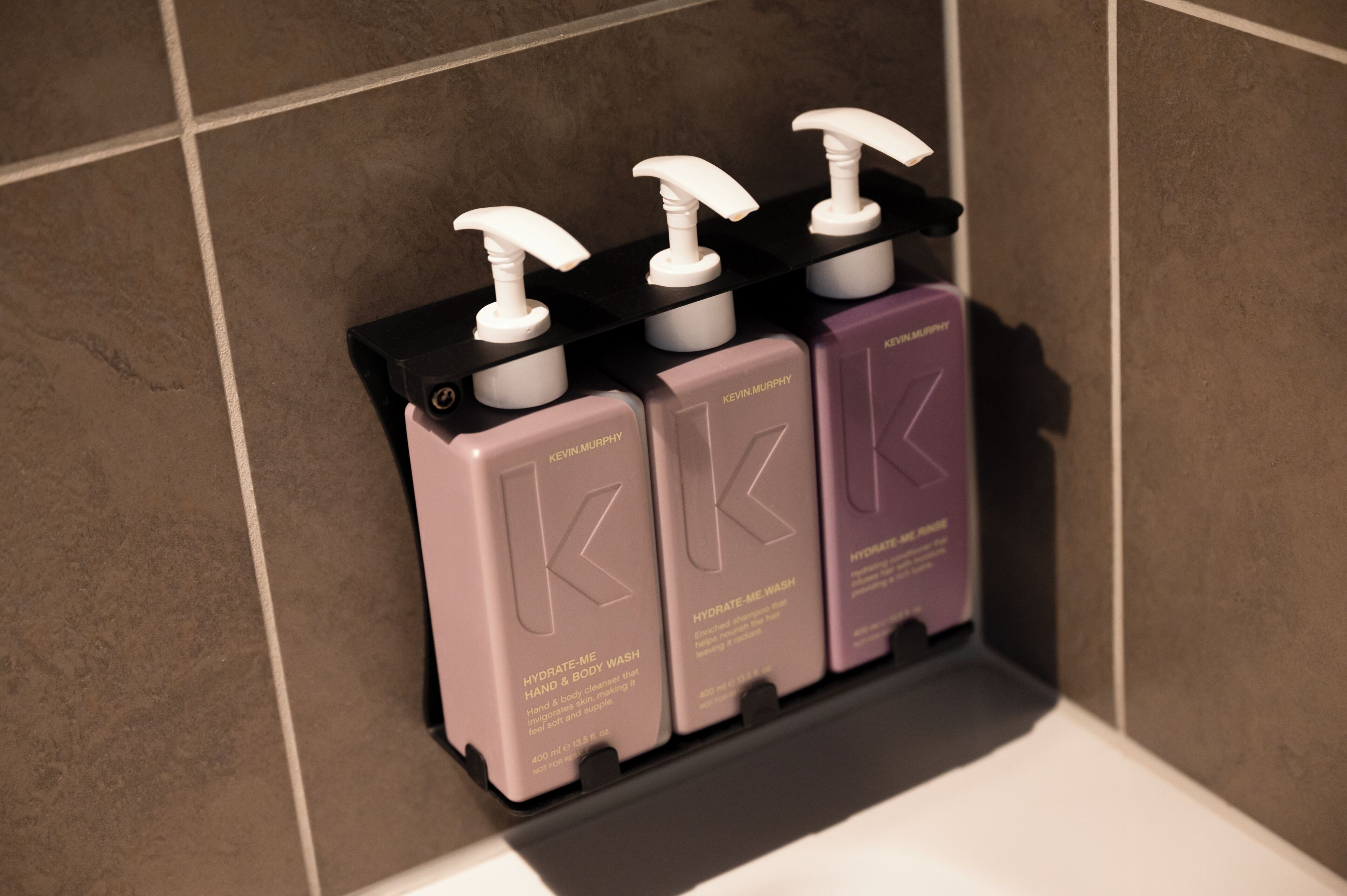 A bathroom shelf with three bottles of Kevin Murphy hand and body wash.