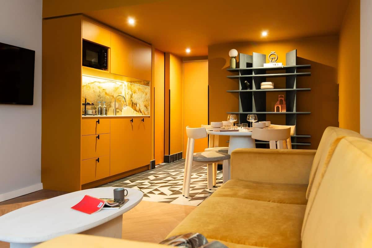 Un salon moderne comprenant un canapé, une table basse, un coin repas avec une table et des chaises, et un coin cuisine avec des placards et un four à micro-ondes.