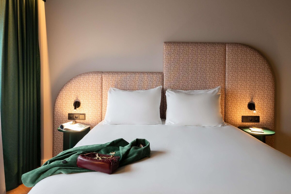 Une chambre d’hôtel avec un grand lit, deux tables de chevet et un rideau vert.