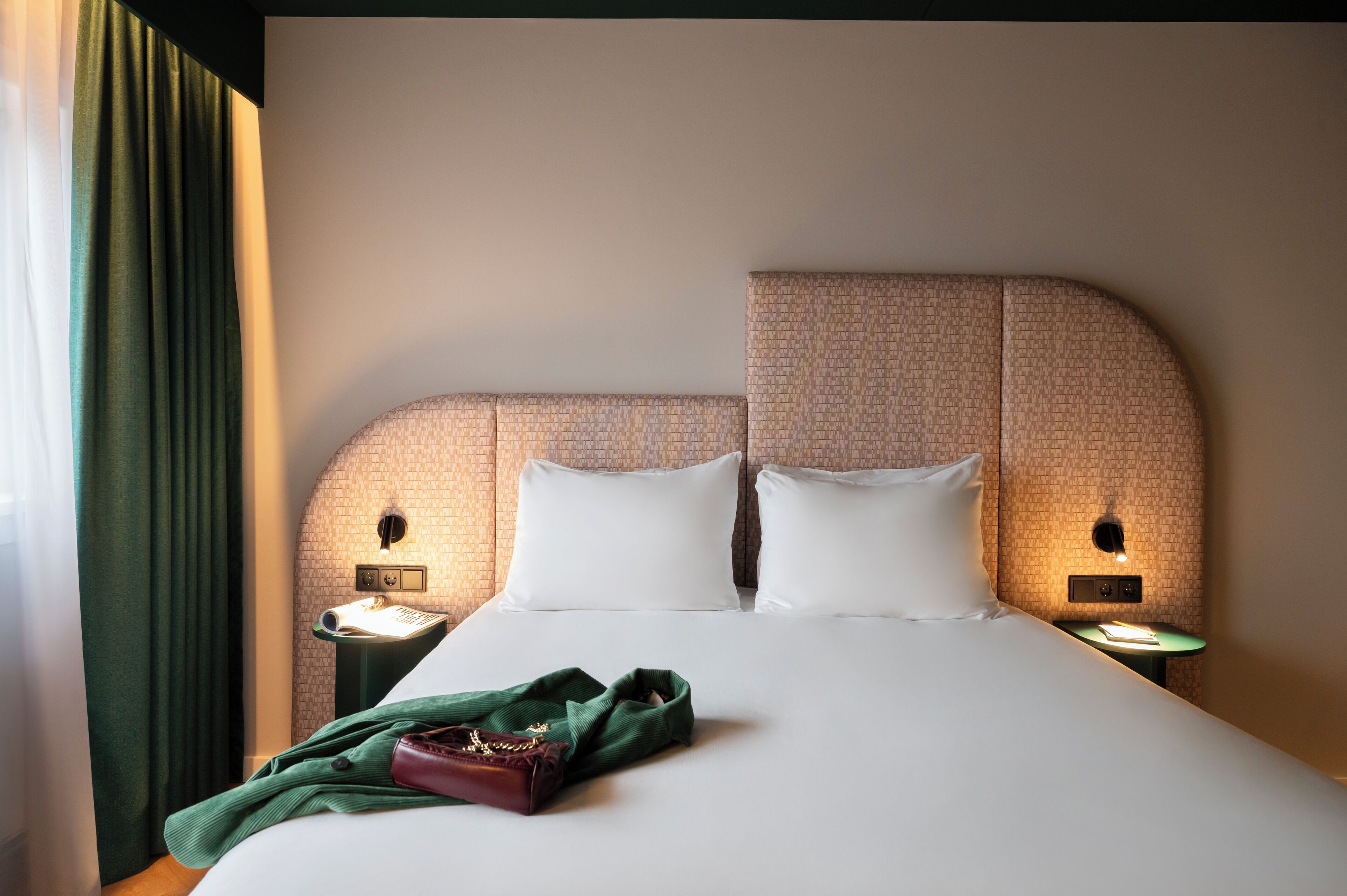 A neatly made bed with white linens, two bedside tables with lamps, and a green curtain.