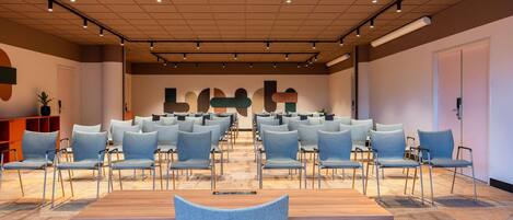 Une salle de conférence avec des rangées de chaises, une table en bois et un tapis à motifs.